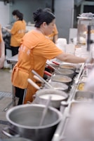Woman in orange shirt preparing food in kitchen.