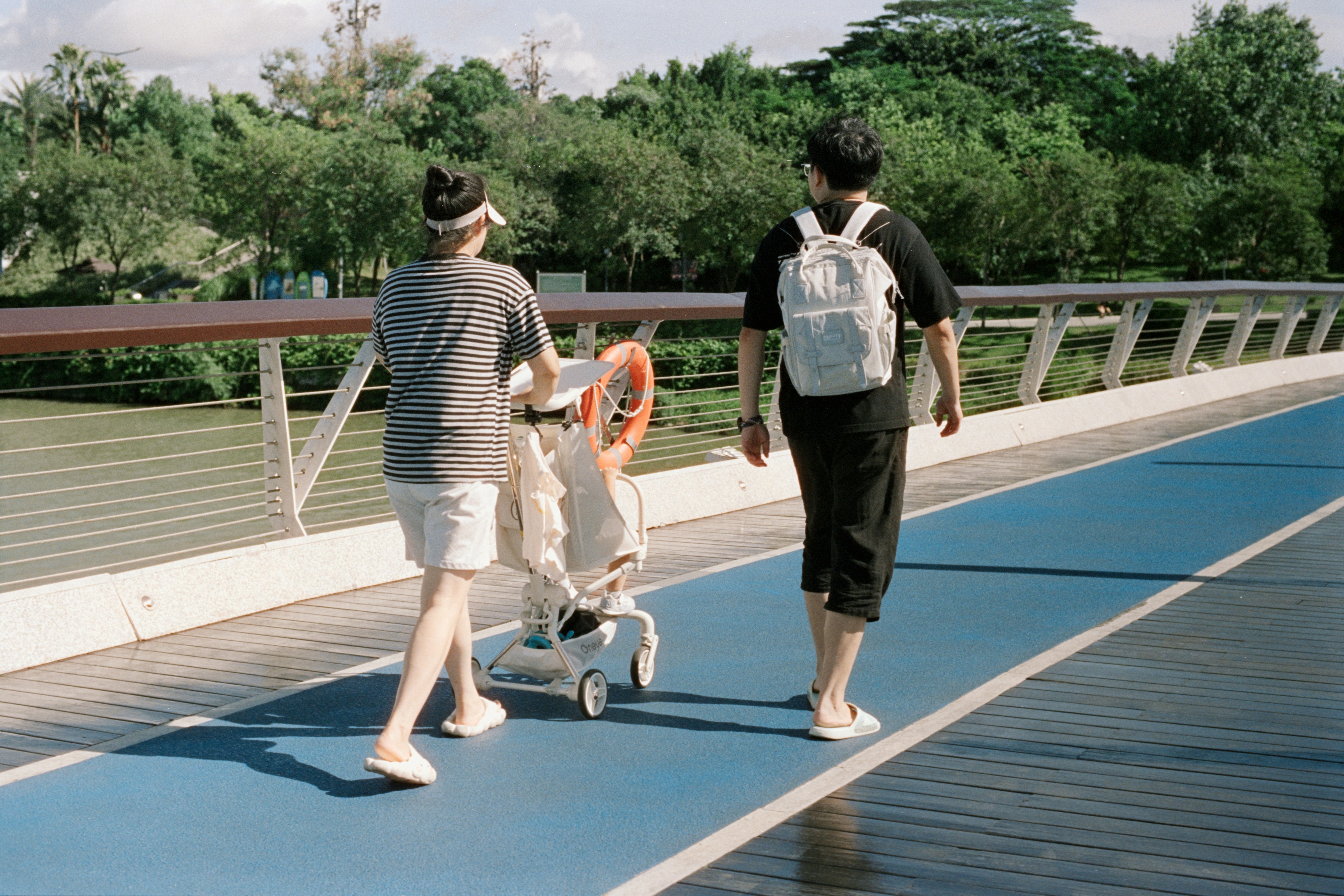 Two people walk with a stroller on a blue path.