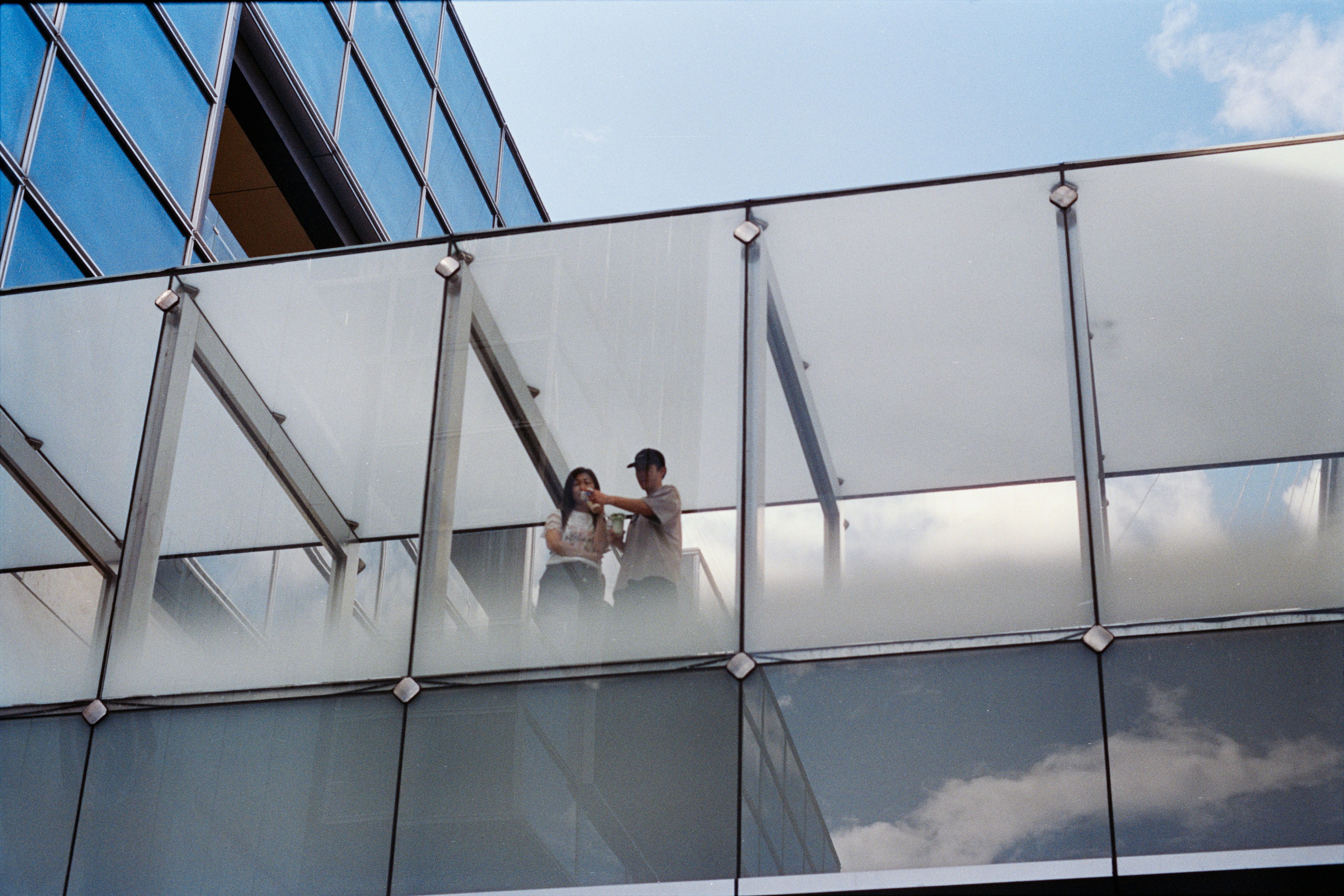 Two people on a glass walkway between buildings