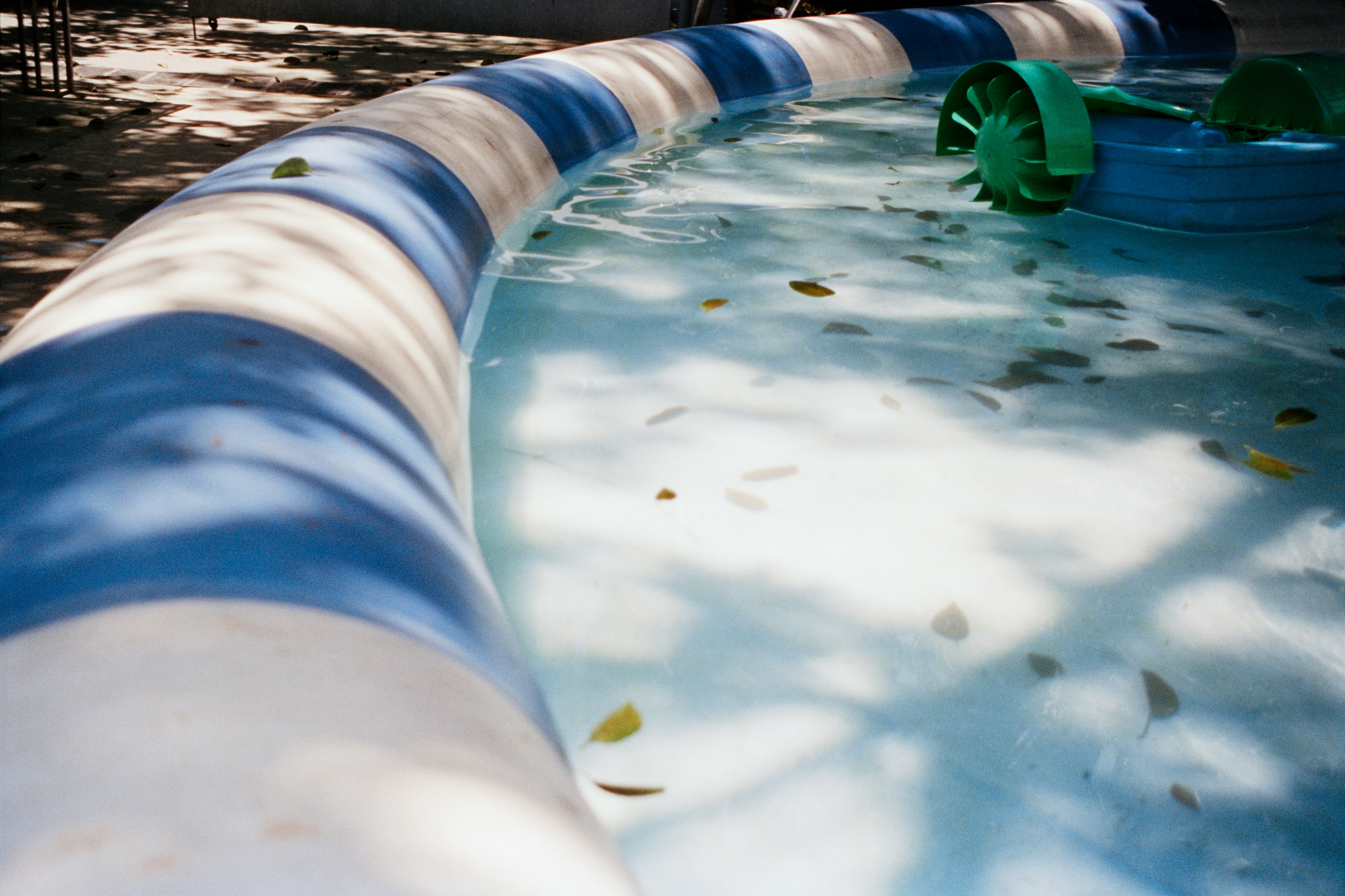 Inflatable pool with scattered leaves and green water wheel.