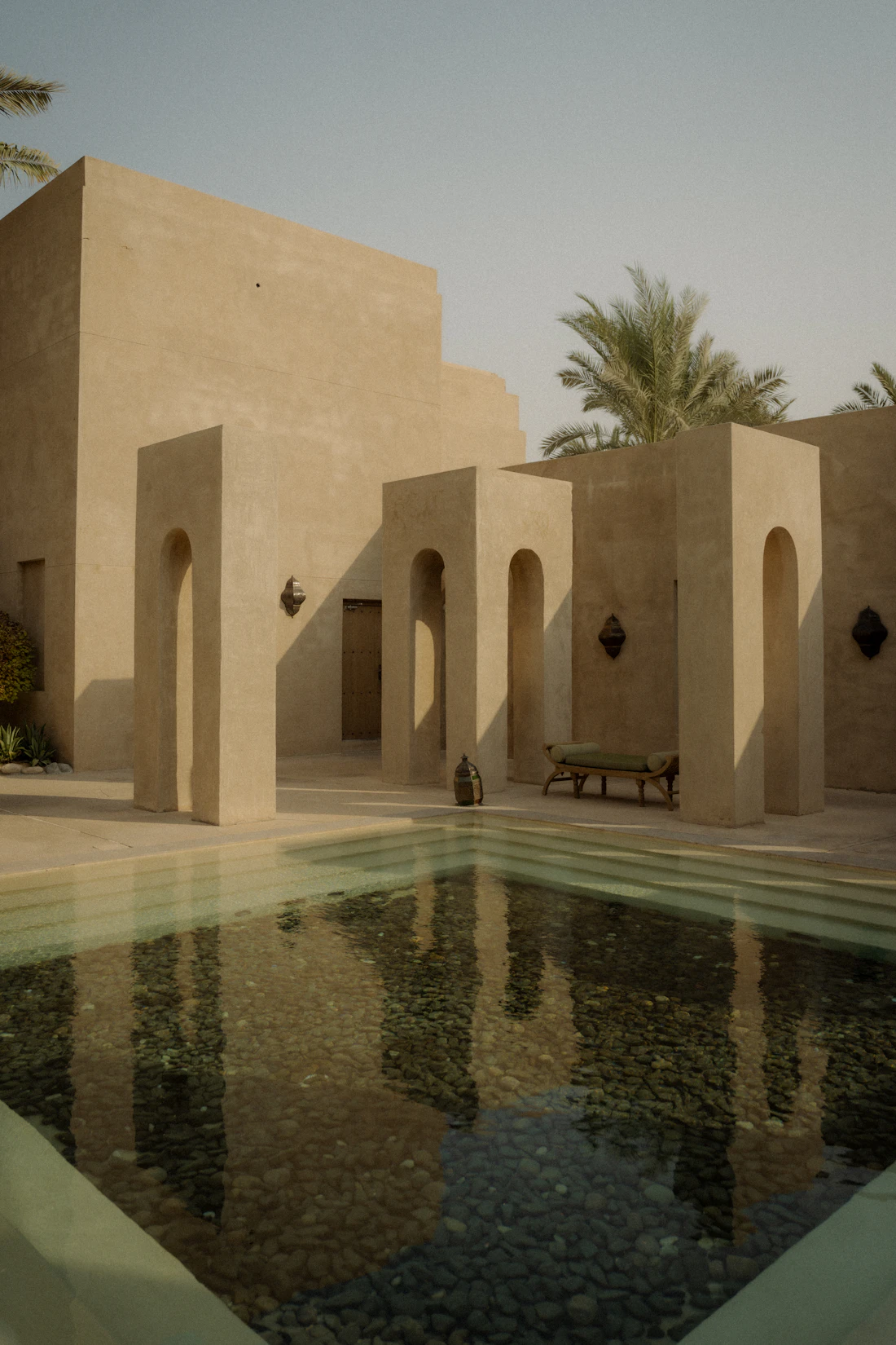 Contemporary lime-plastered house with arched openings reflected in a still pool