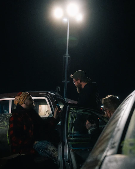Three men talking near cars at night