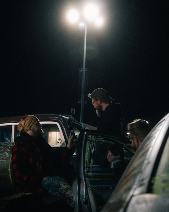 Three men talking near cars at night