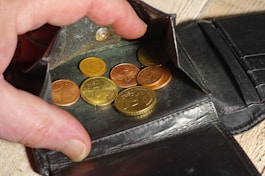 Hand placing coins into a black leather wallet.