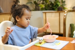 Young child eating with a pink spoon and bowl.