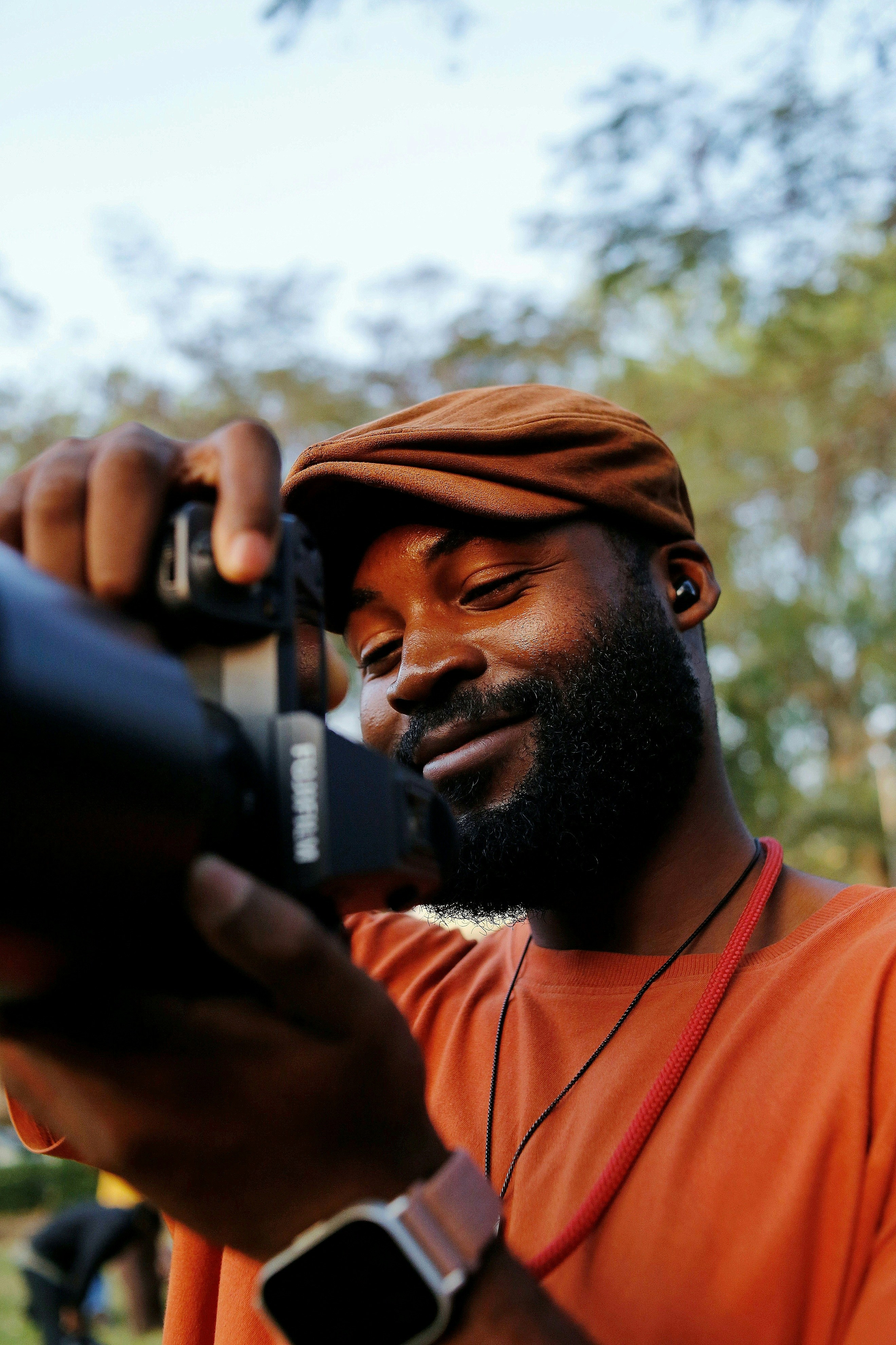Mann mit Schiebermütze und orangefarbenem Hemd mit Kamera