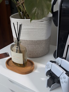 Reed diffuser on wooden tray next to game controllers.
