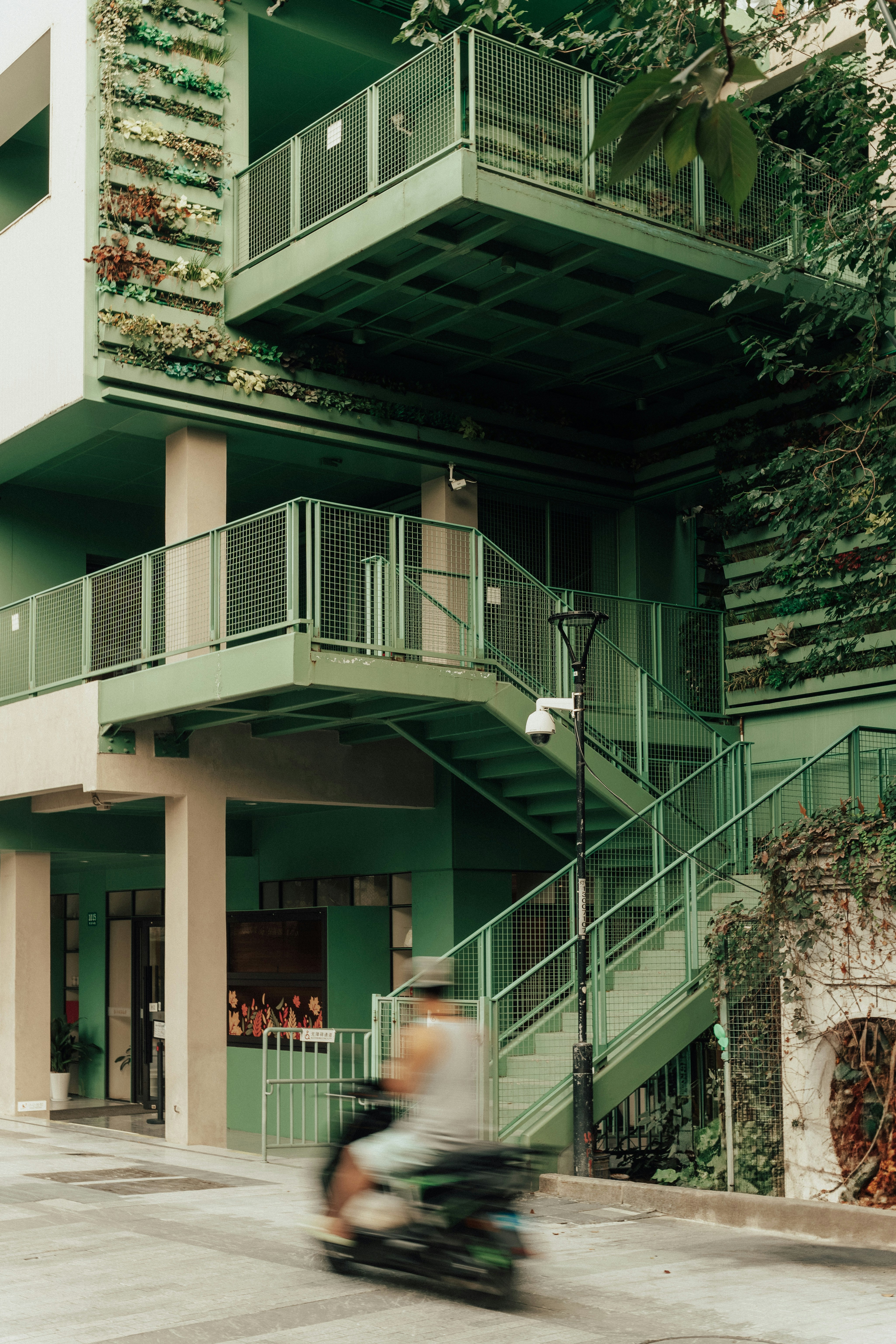 Green building with outdoor staircase and scooter passing by.