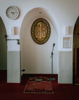 Prayer rug and microphone in front of islamic calligraphy.