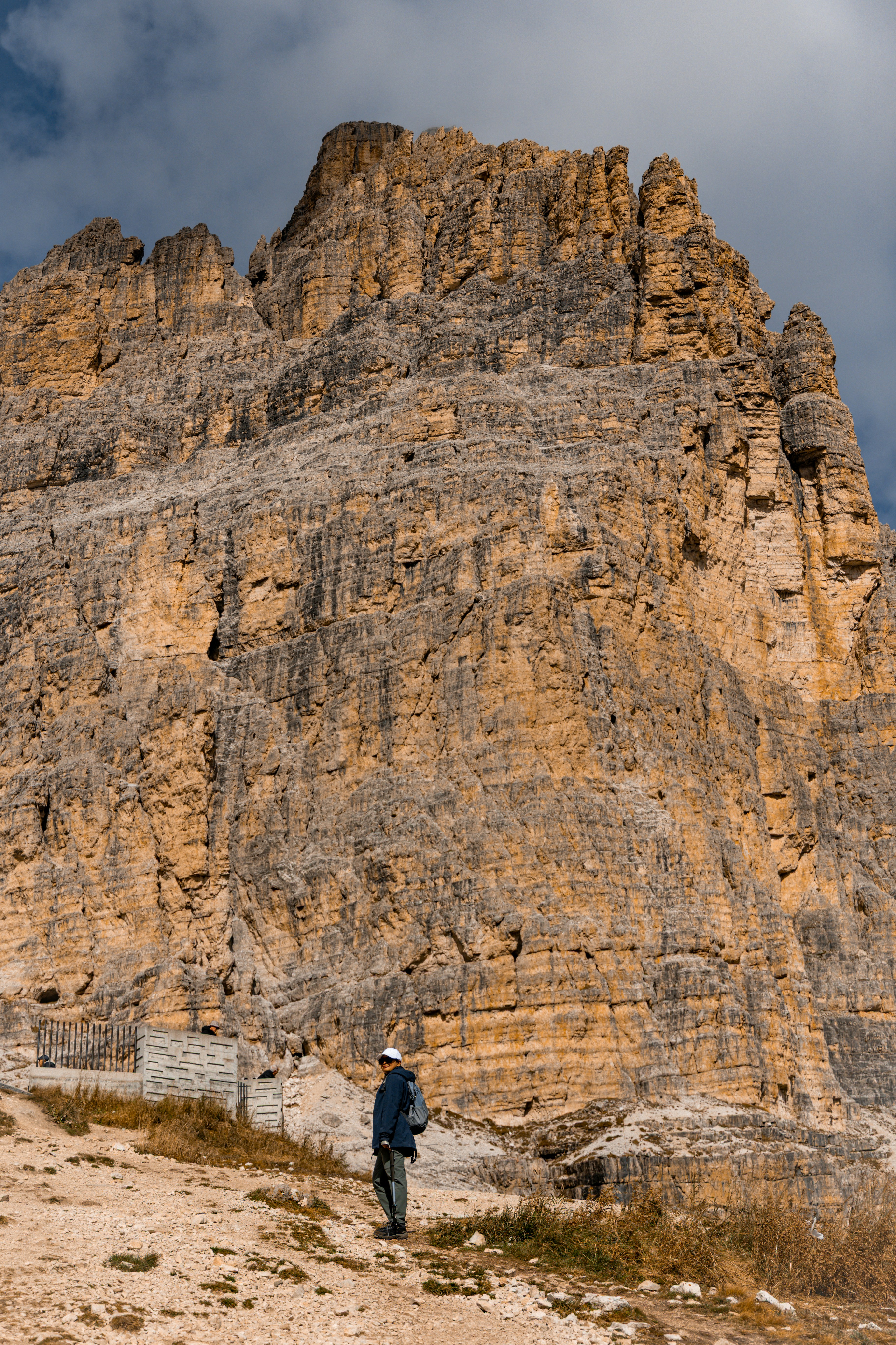 A person stands before a massive, rocky mountain face.