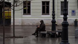 Person in hooded jacket sitting on bench outdoors