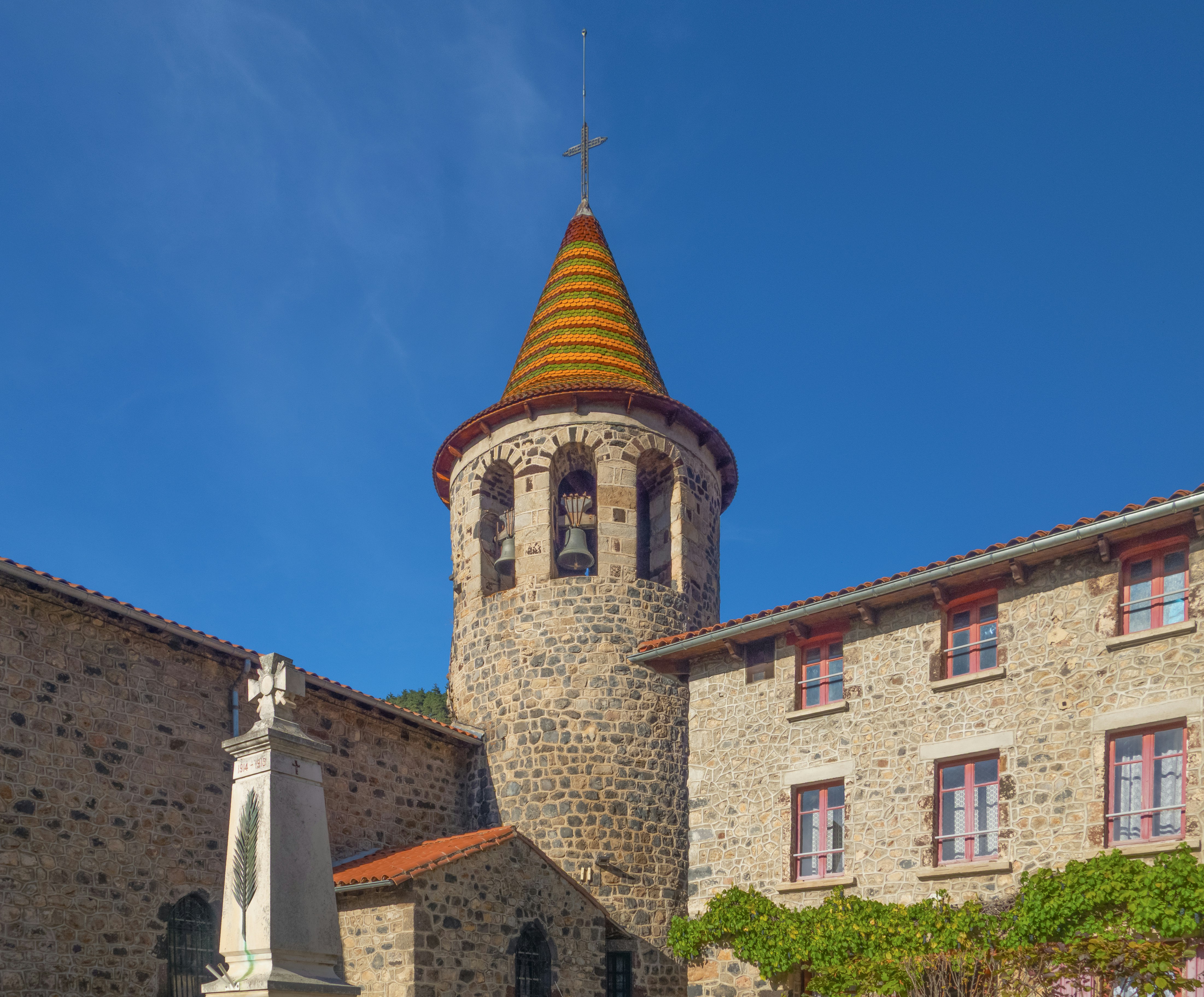 Stone church tower with yellow conical roof against blue sky.
