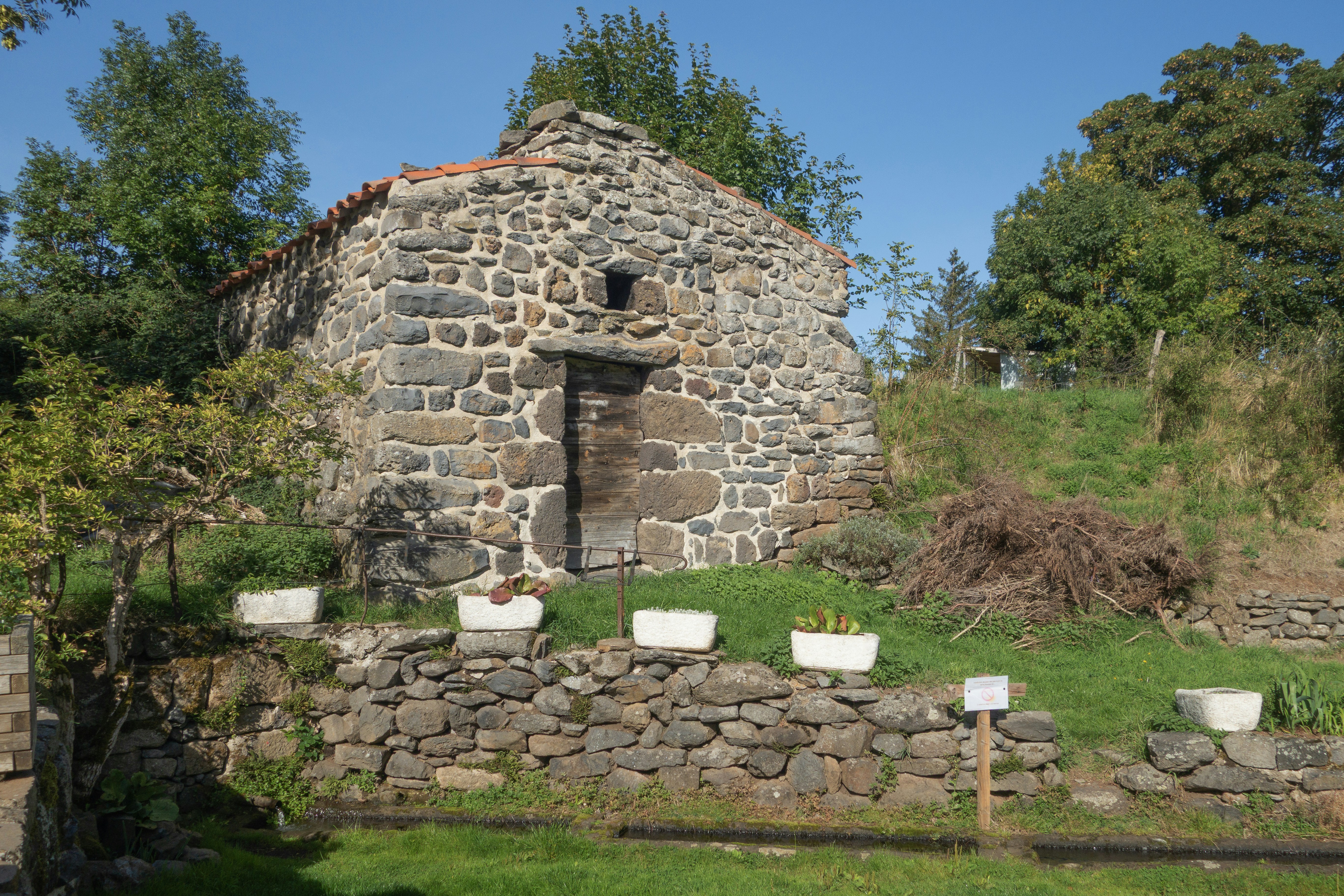 Old stone building with a wooden door in a garden.