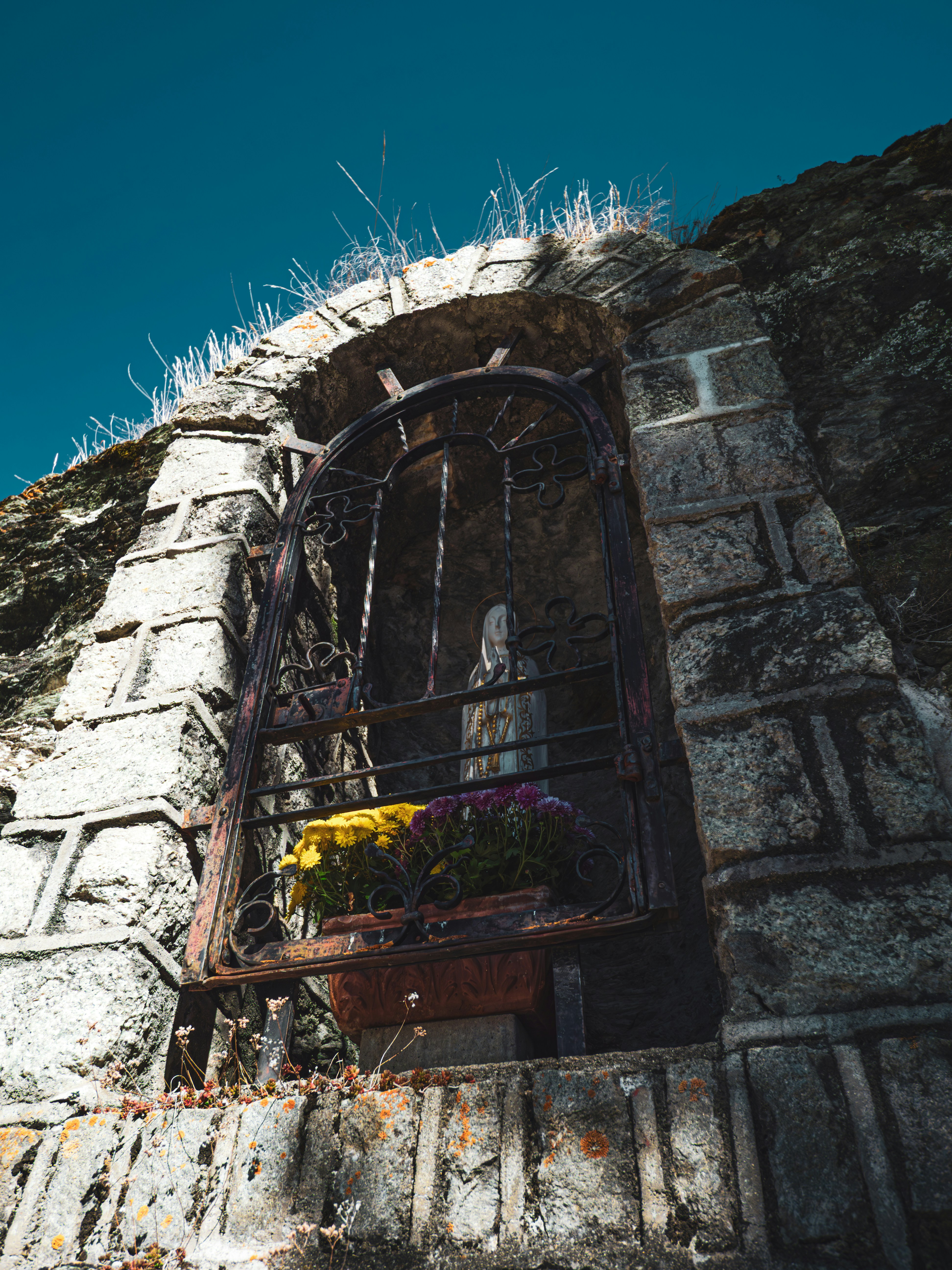 Stone niche with flowers and statue under blue sky