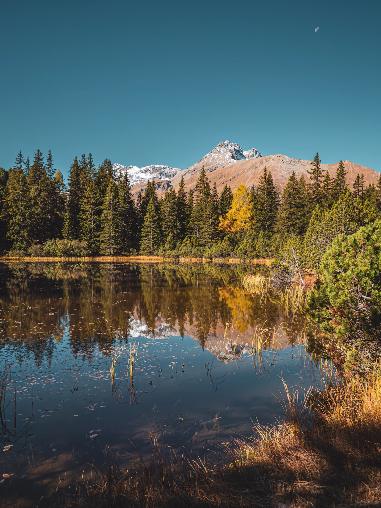 Mountain lake reflecting alpine peaks and autumn trees.