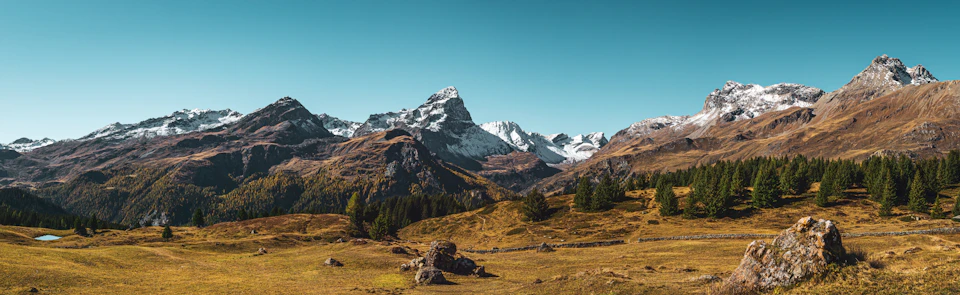 Breathtaking mountain range under clear blue sky with snow-covered peaks and scattered rocks