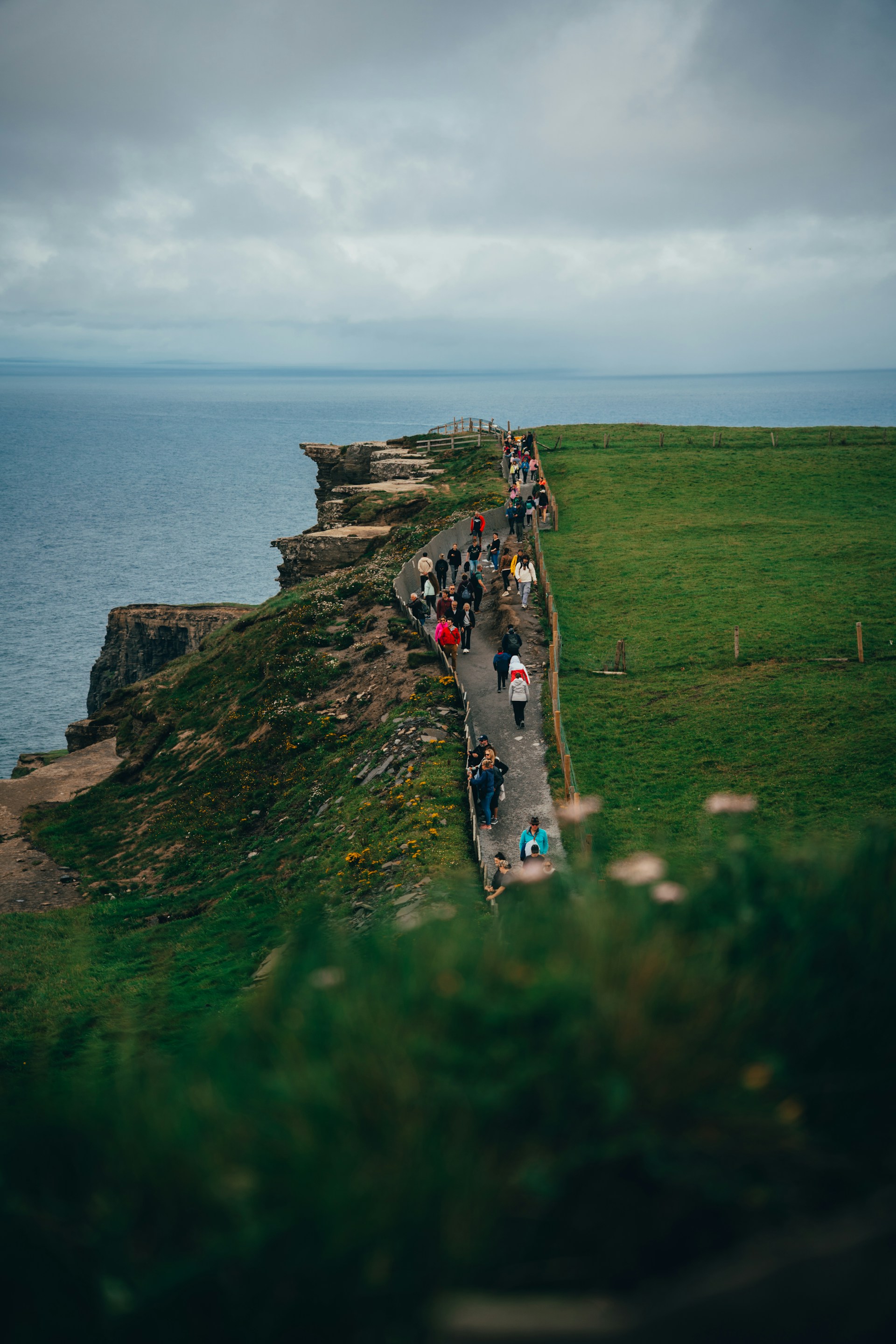 Tourists walk along a cliff path beside the ocean.