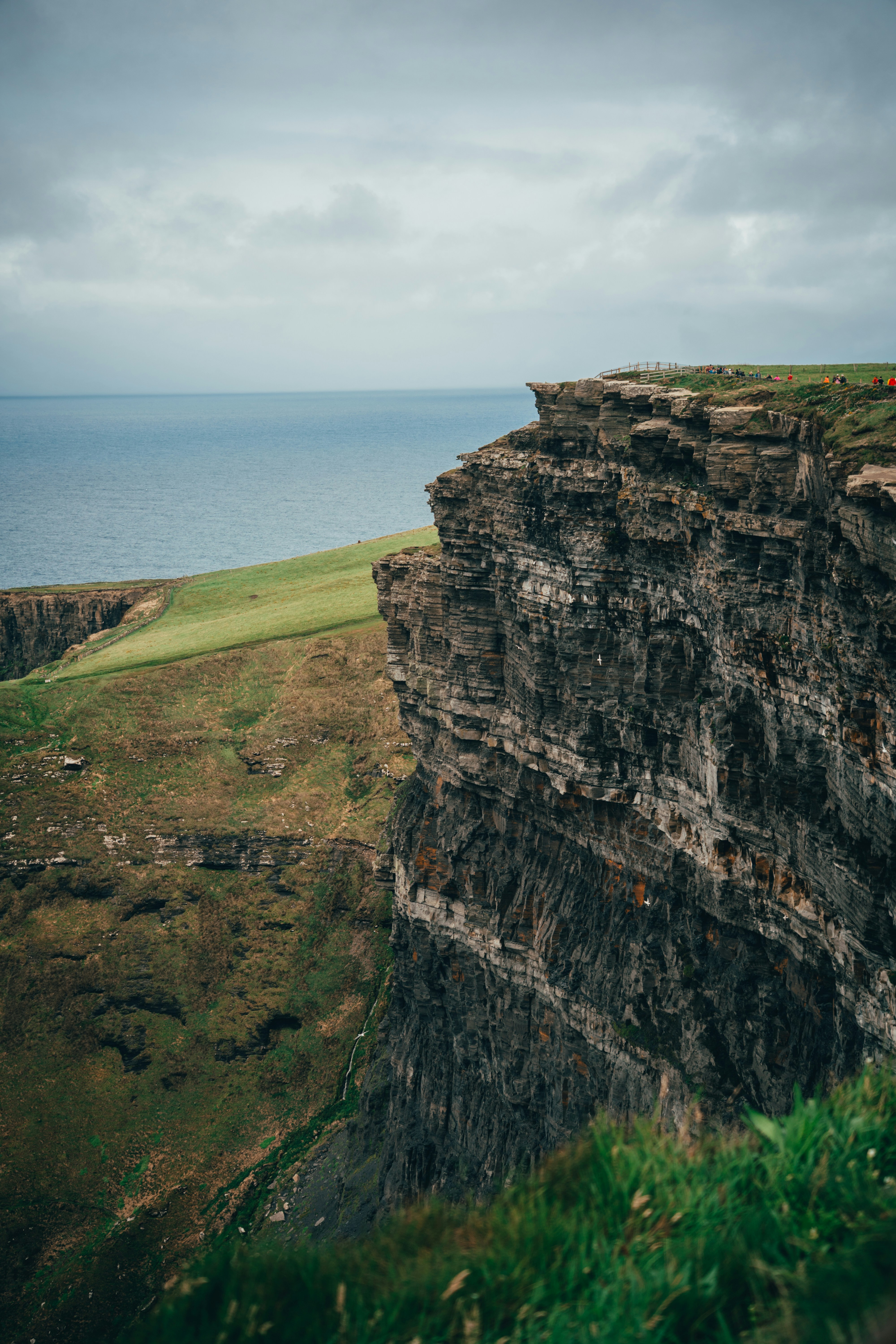 Los escarpados acantilados dominan un vasto océano azul bajo cielos nublados.
