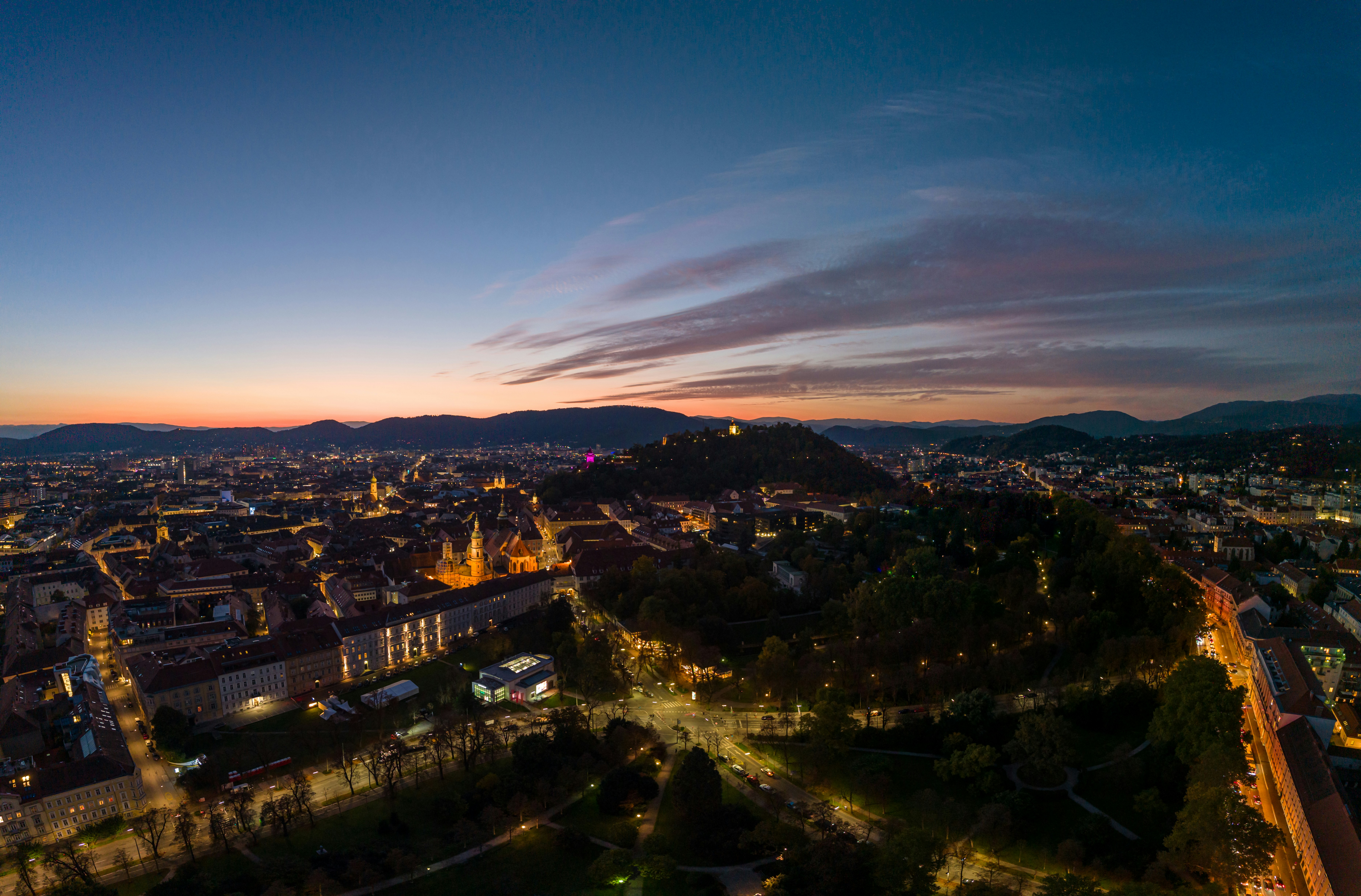 Cityscape with hills at dusk with scattered lights.