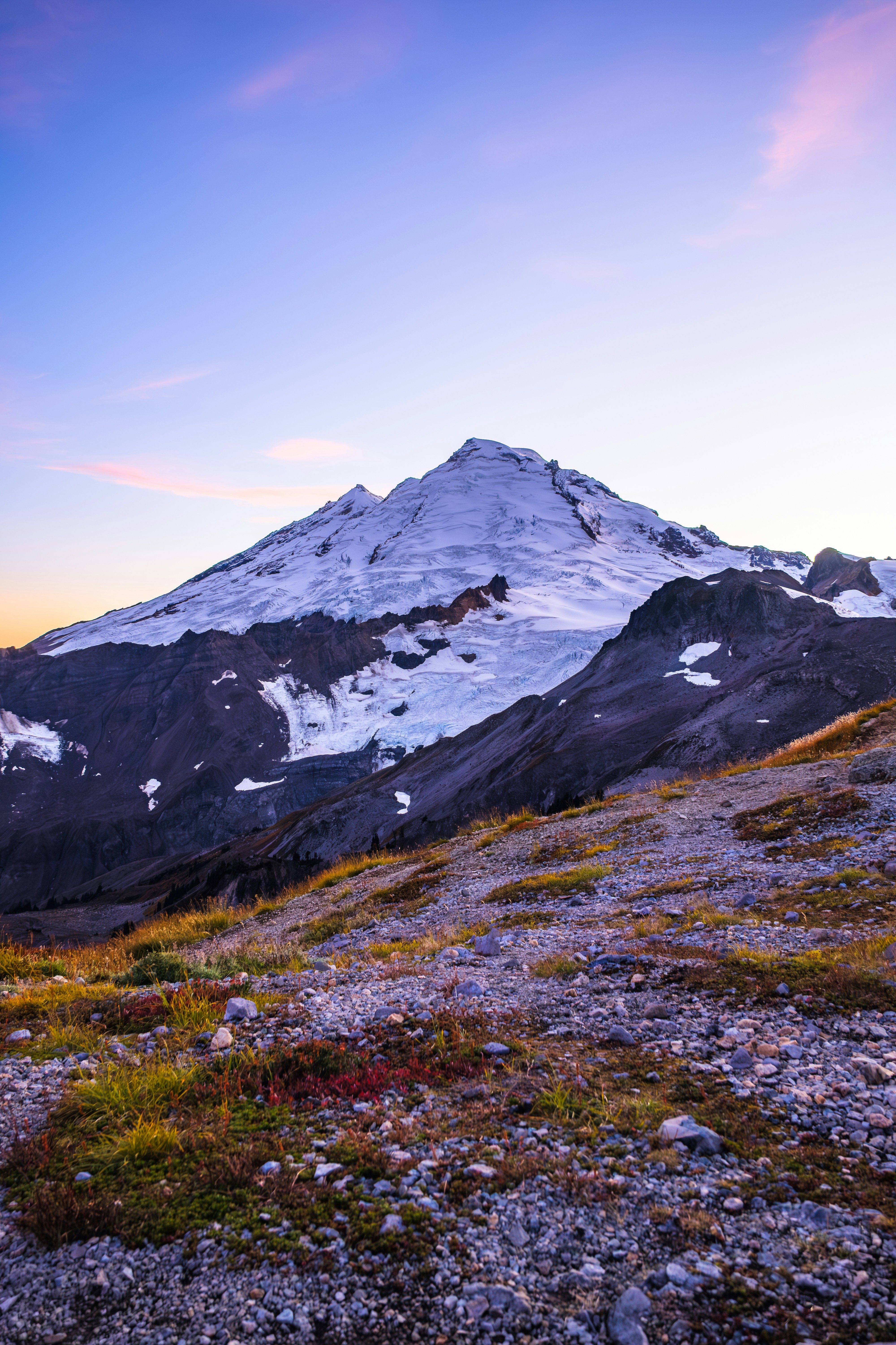 Snow-covered mountain peak at sunrise with purple sky.