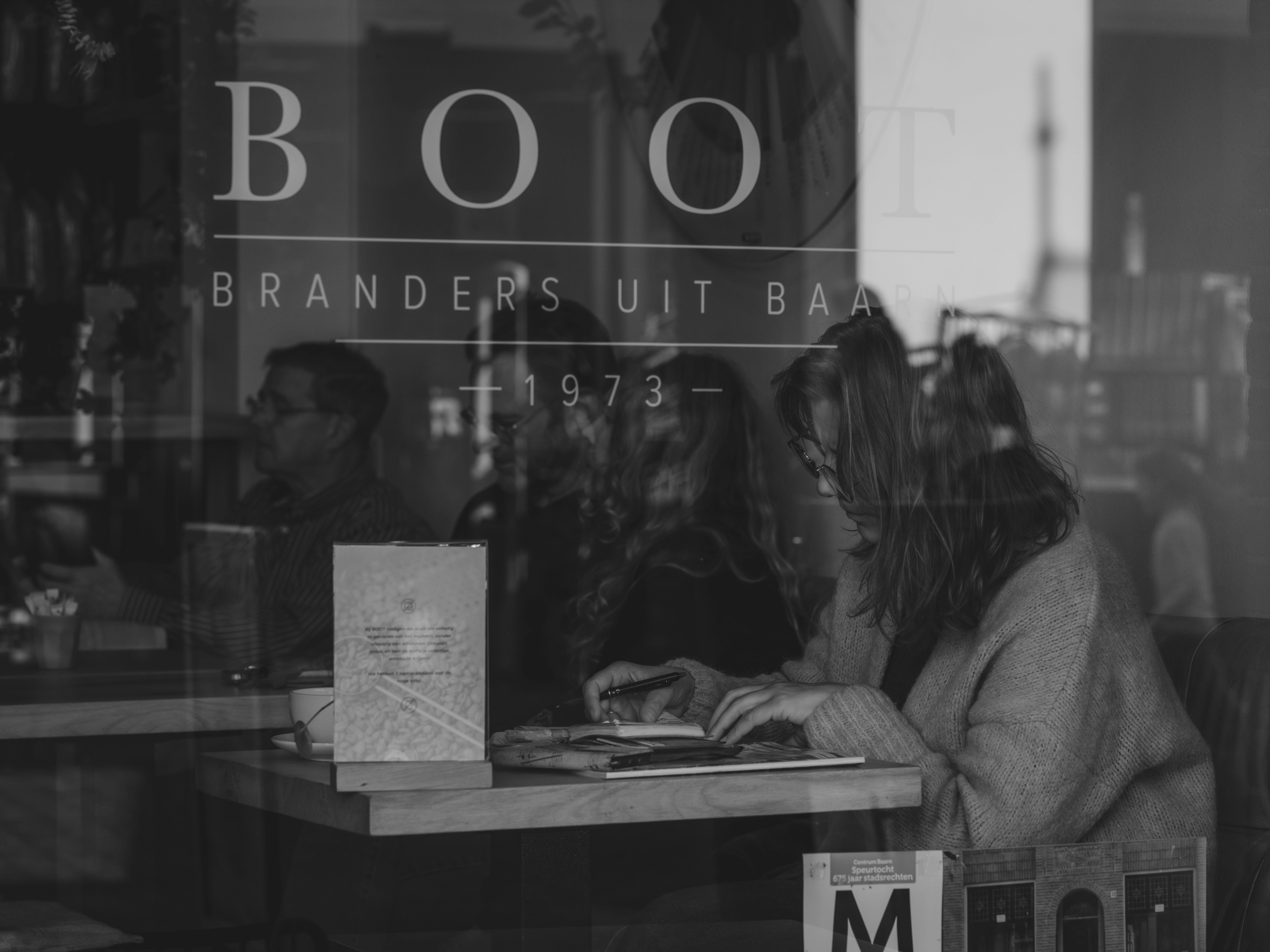 People reflected in a bookstore window with "boot" sign.