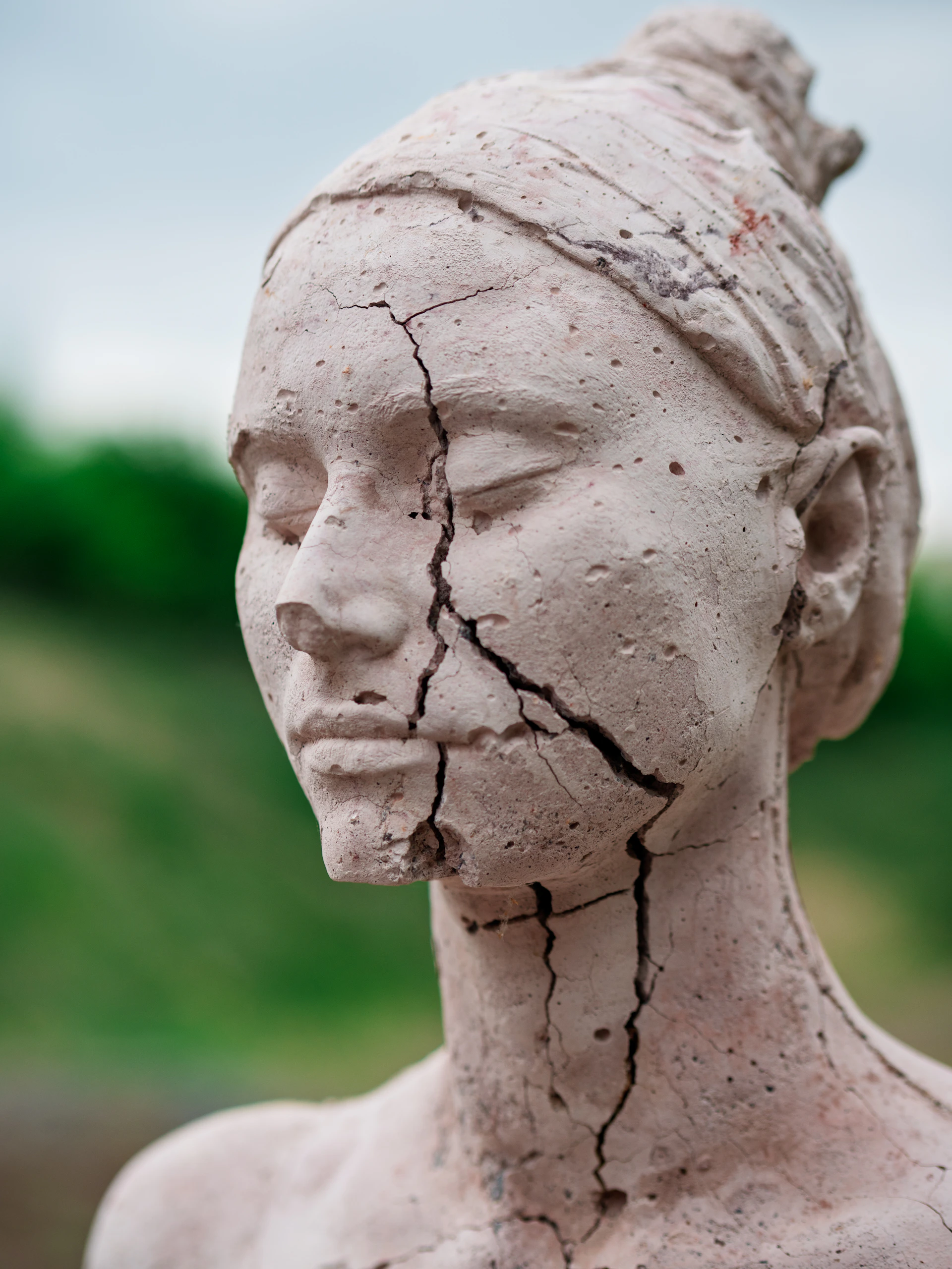 A cracked stone sculpture of a woman's head outdoors.