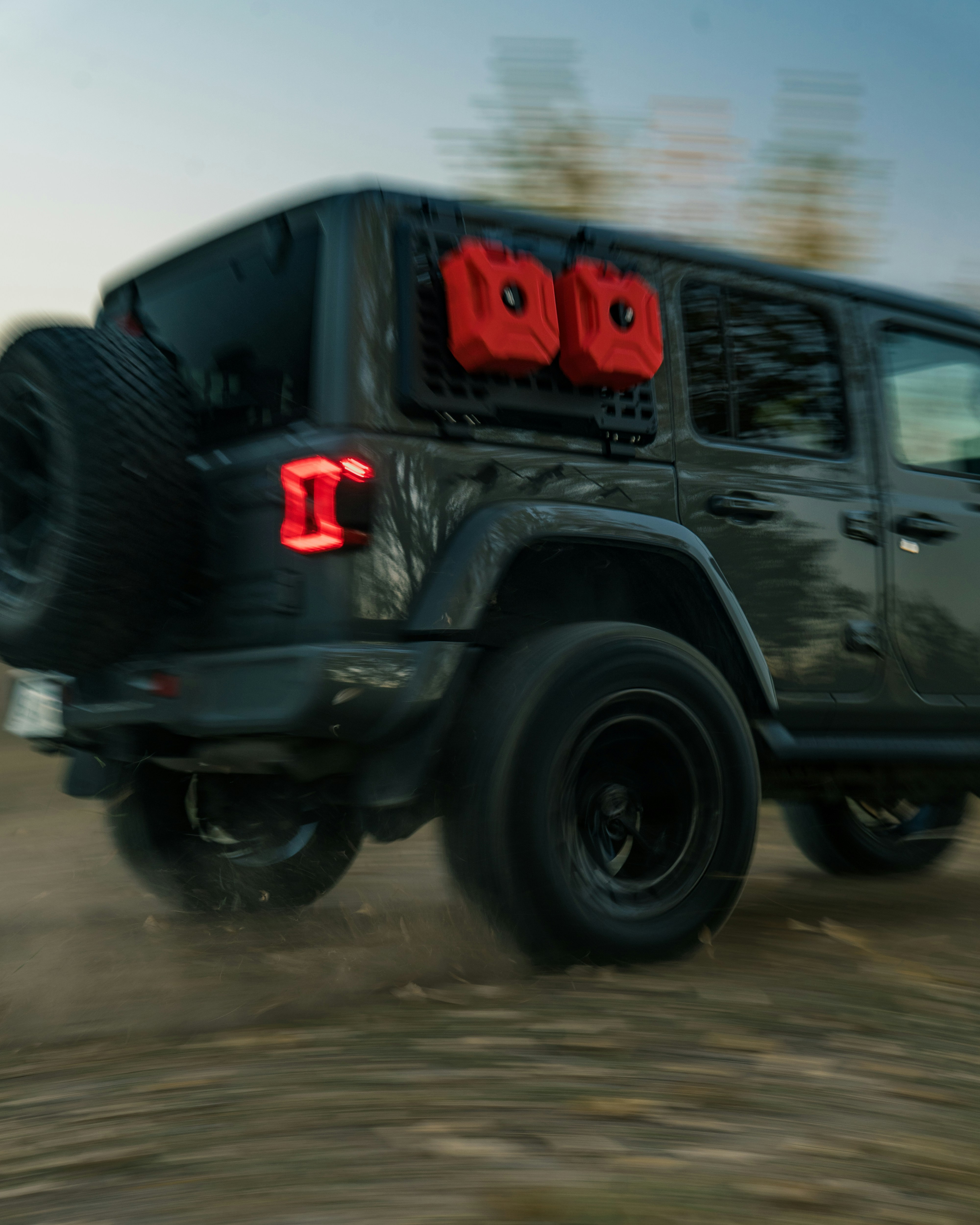 Dark jeep wrangler with red gas cans on back