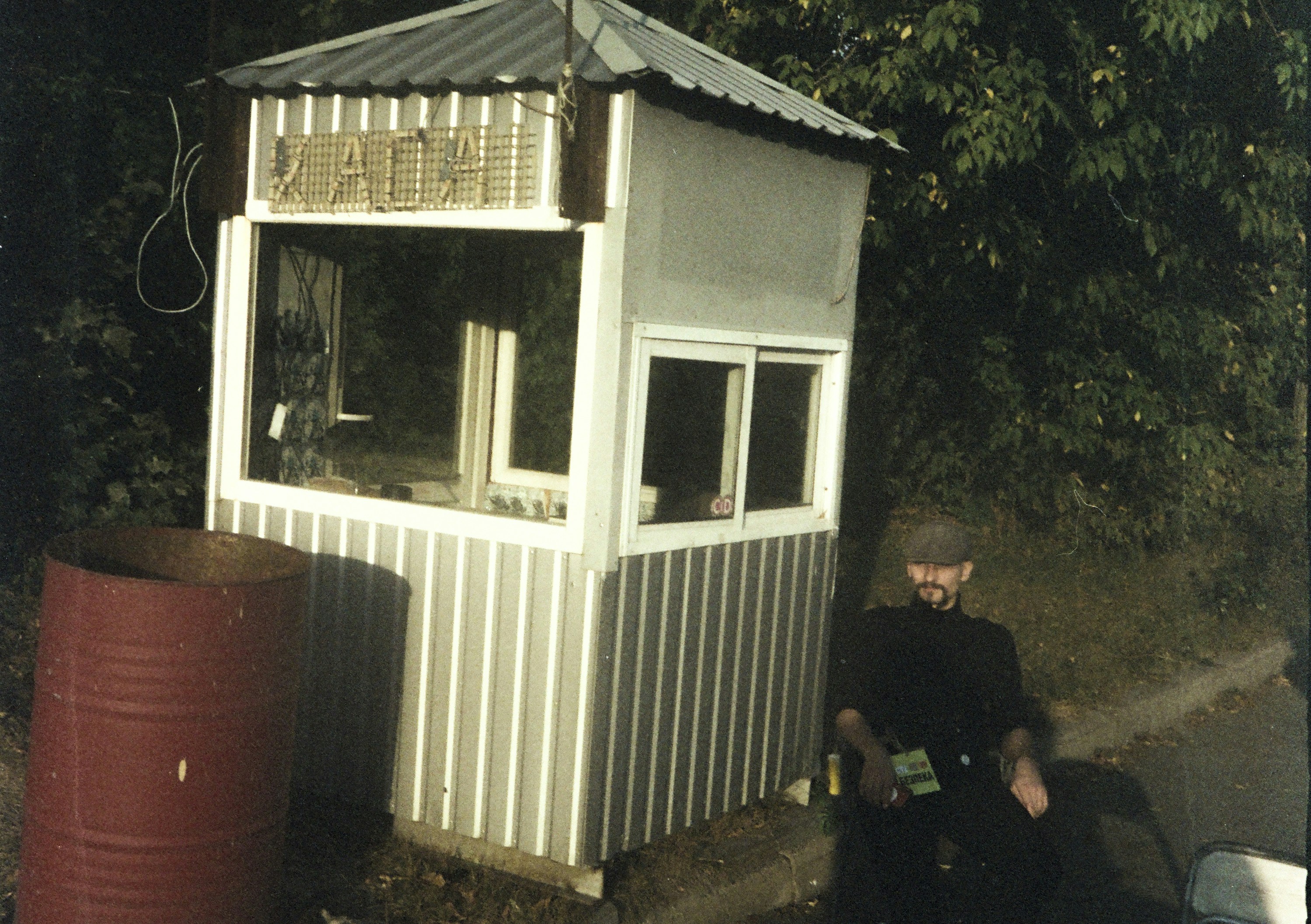 Man in uniform sits by guardhouse with sign.