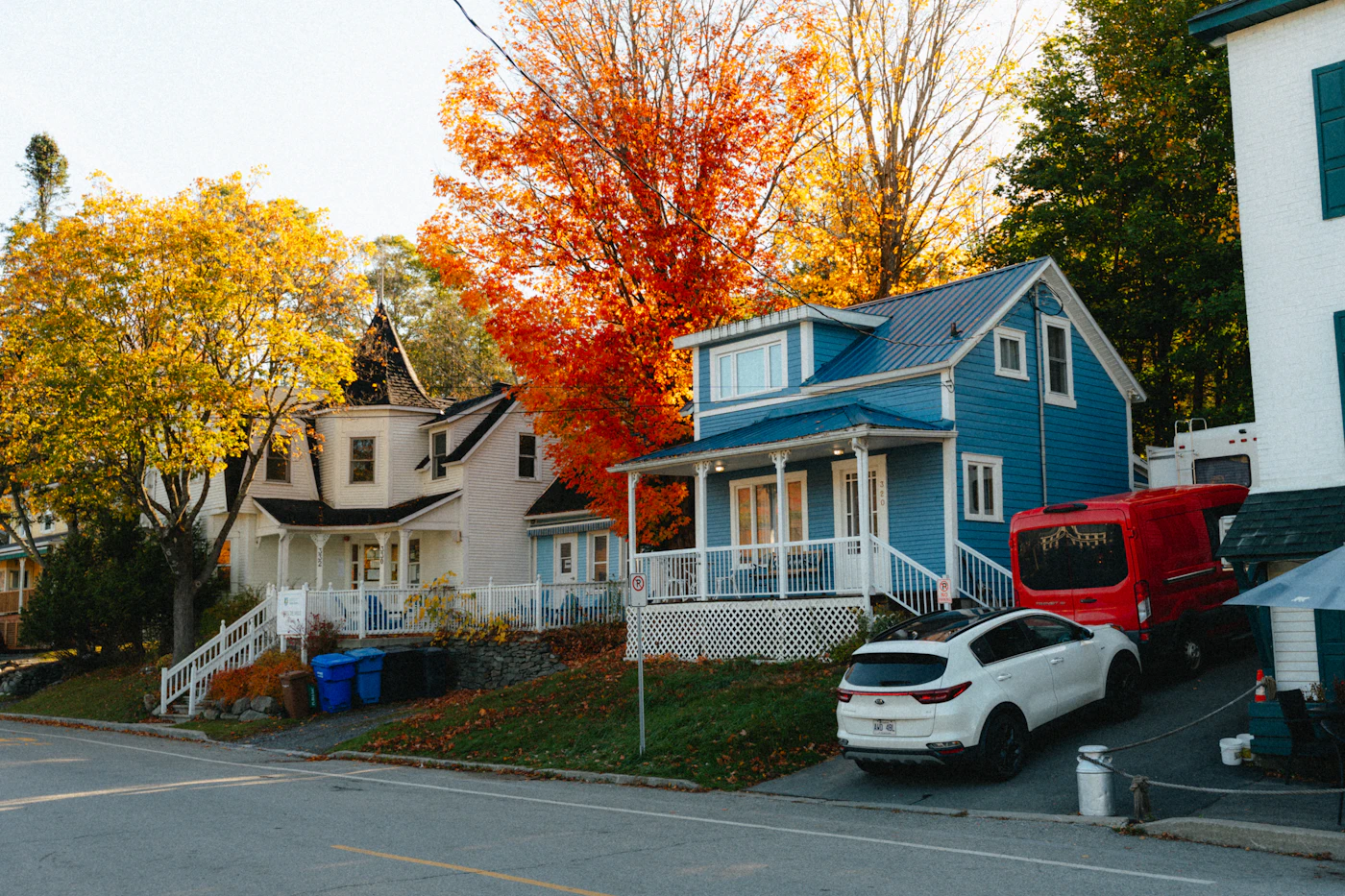 Blue house with a front porch on a street lined with fall trees