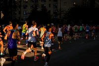 A pack of marathon runners seen from behind on a city street in low evening sun
