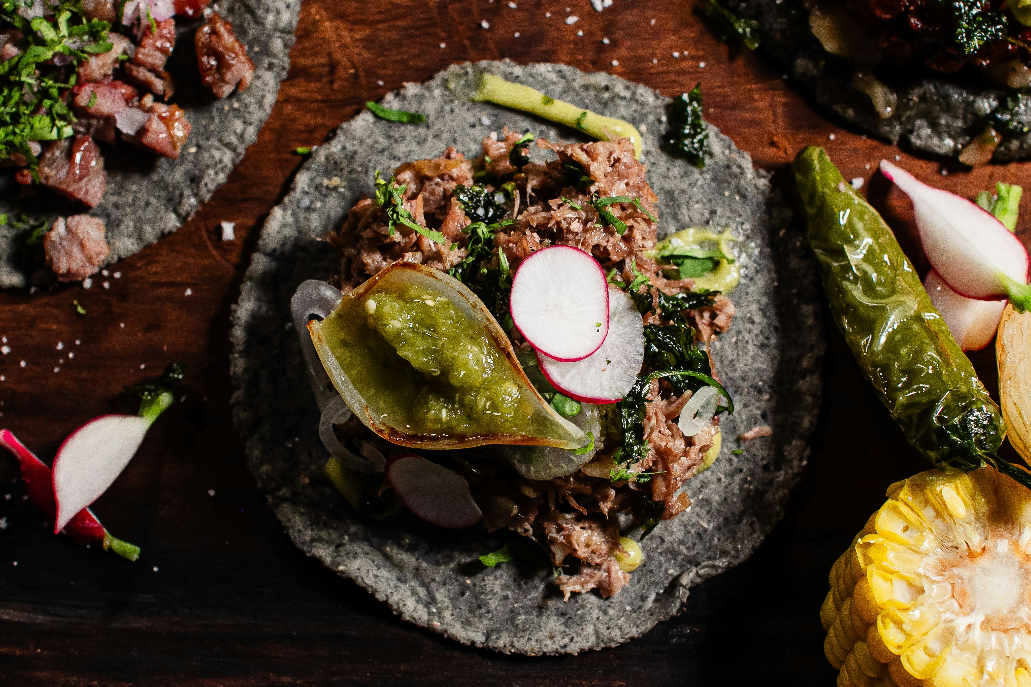 Tacos with meat, vegetables, and salsa on blue corn tortillas.