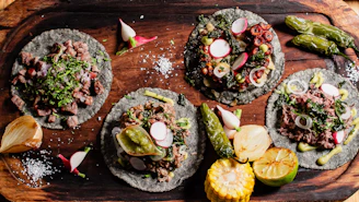 Four gourmet tacos with assorted toppings on wooden board