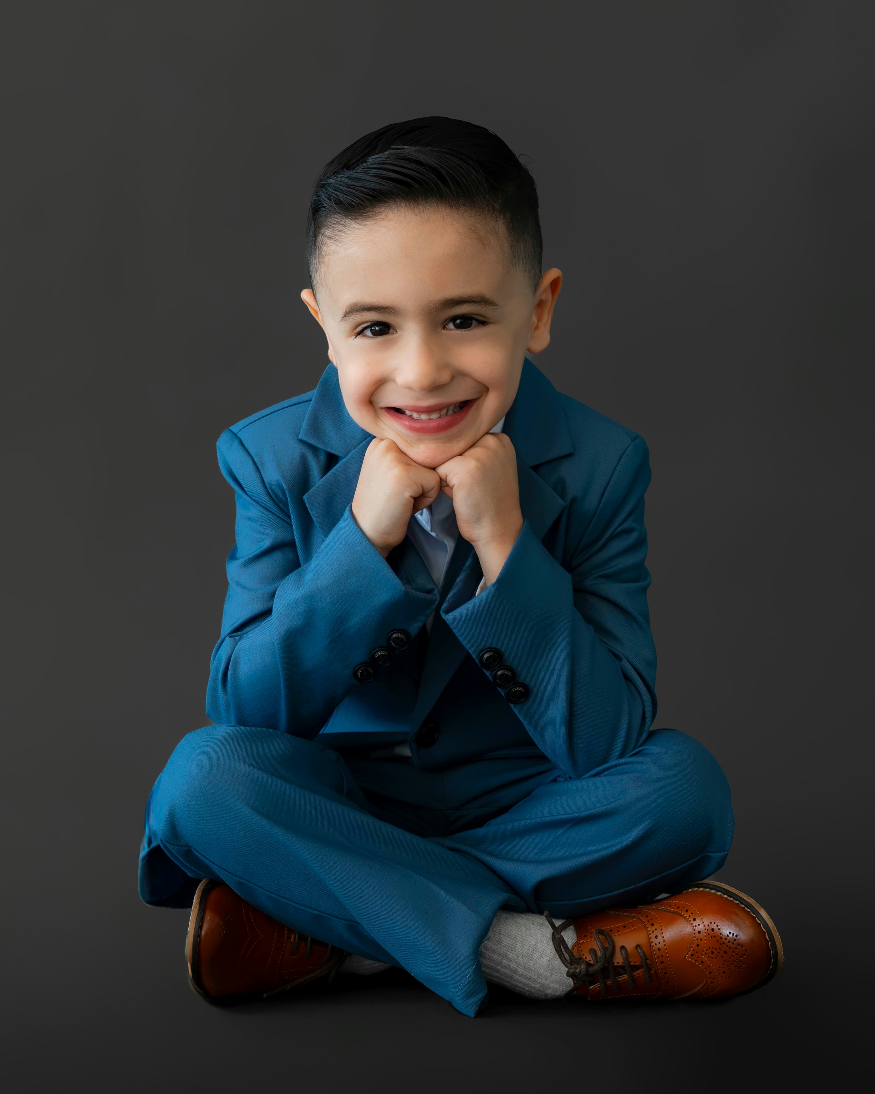 Un jeune garçon en costume bleu sourit joyeusement.