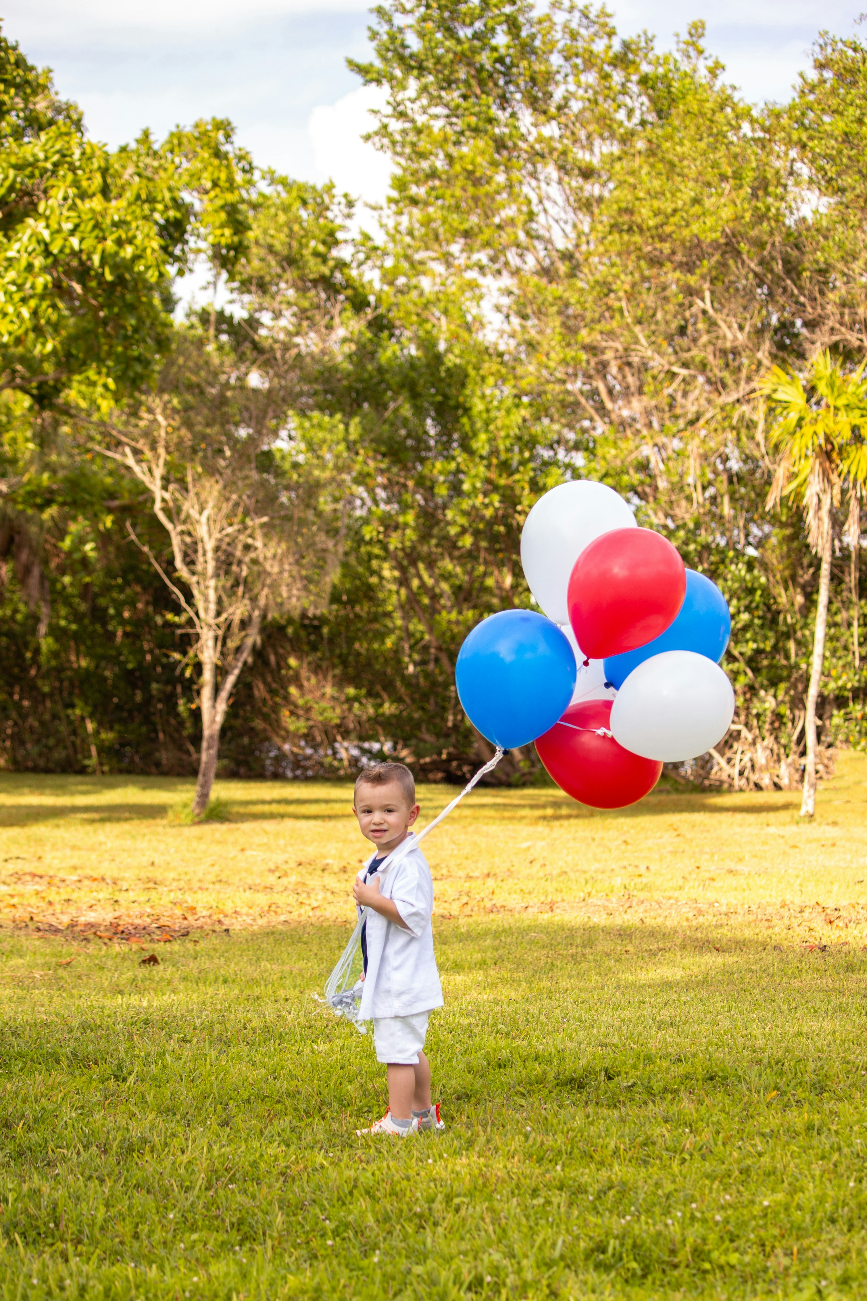 Young boy holding red, white, and blue balloons outdoors