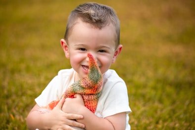 A smiling young boy holding a colorful stuffed toy.