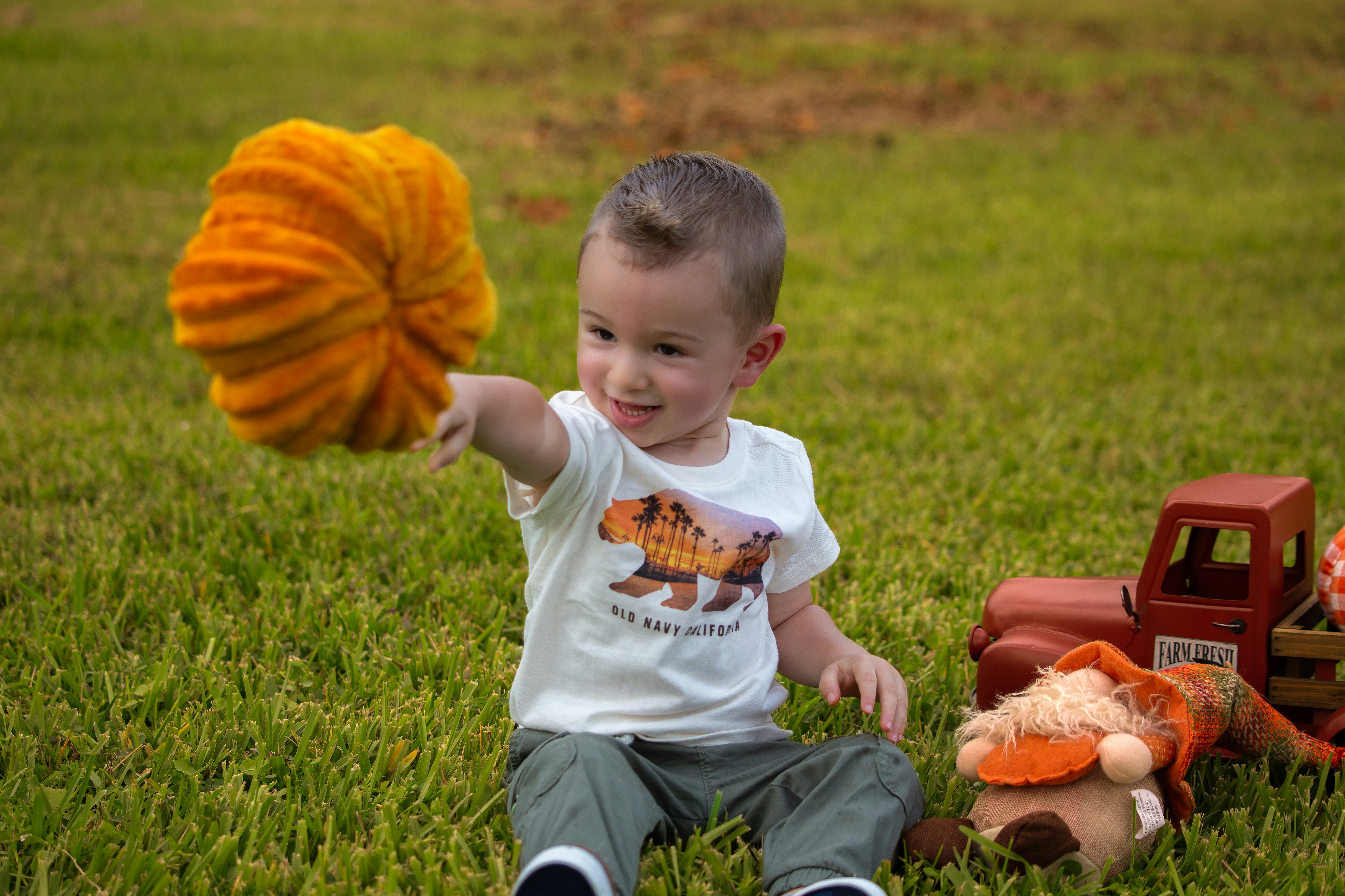 Toddler holding knitted pumpkin with toy truck nearby