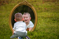 A baby smiles at their reflection in a mirror.