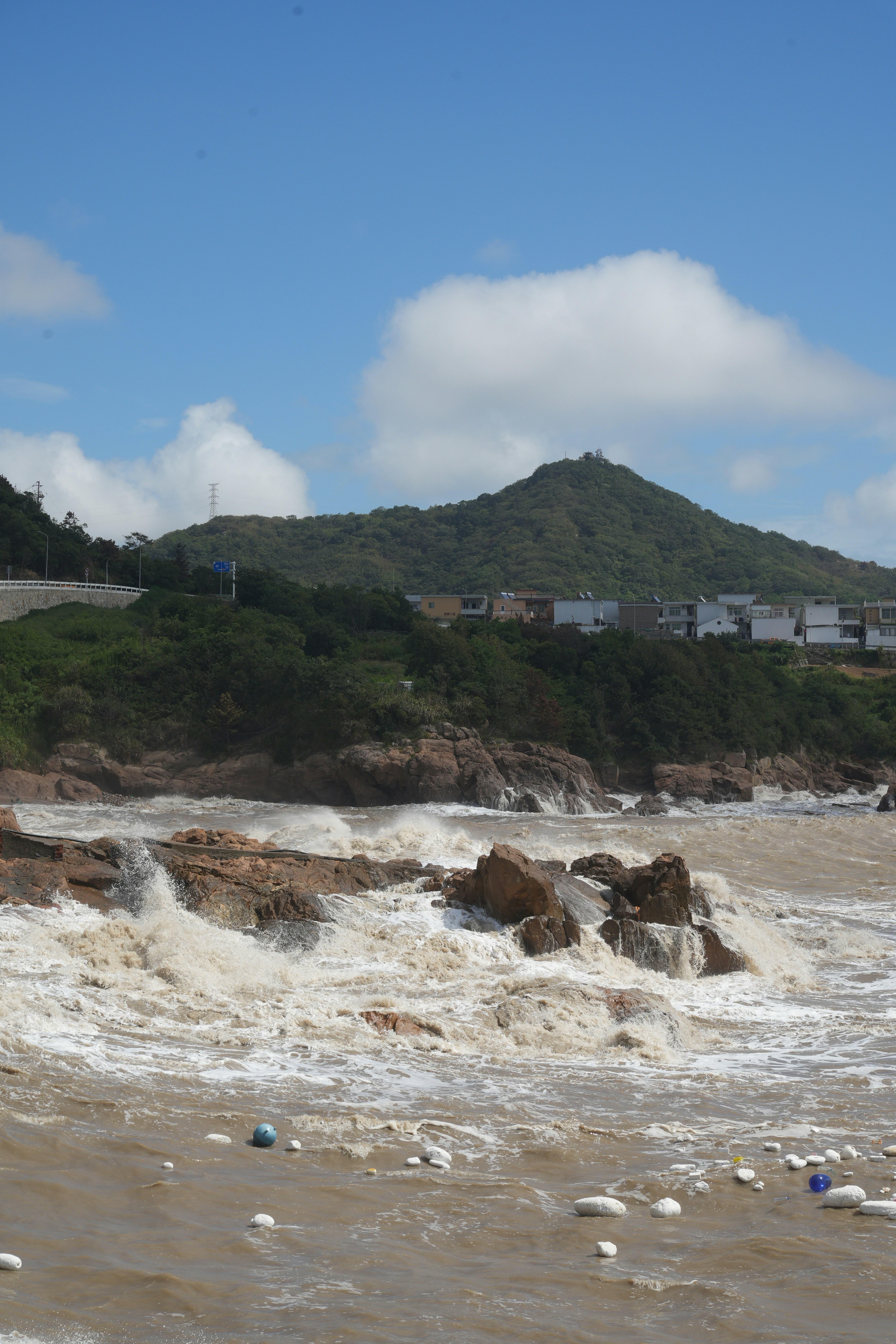 Waves crash against rocky shore with distant green hills.