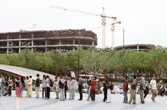 People stand in line near construction site with cranes.