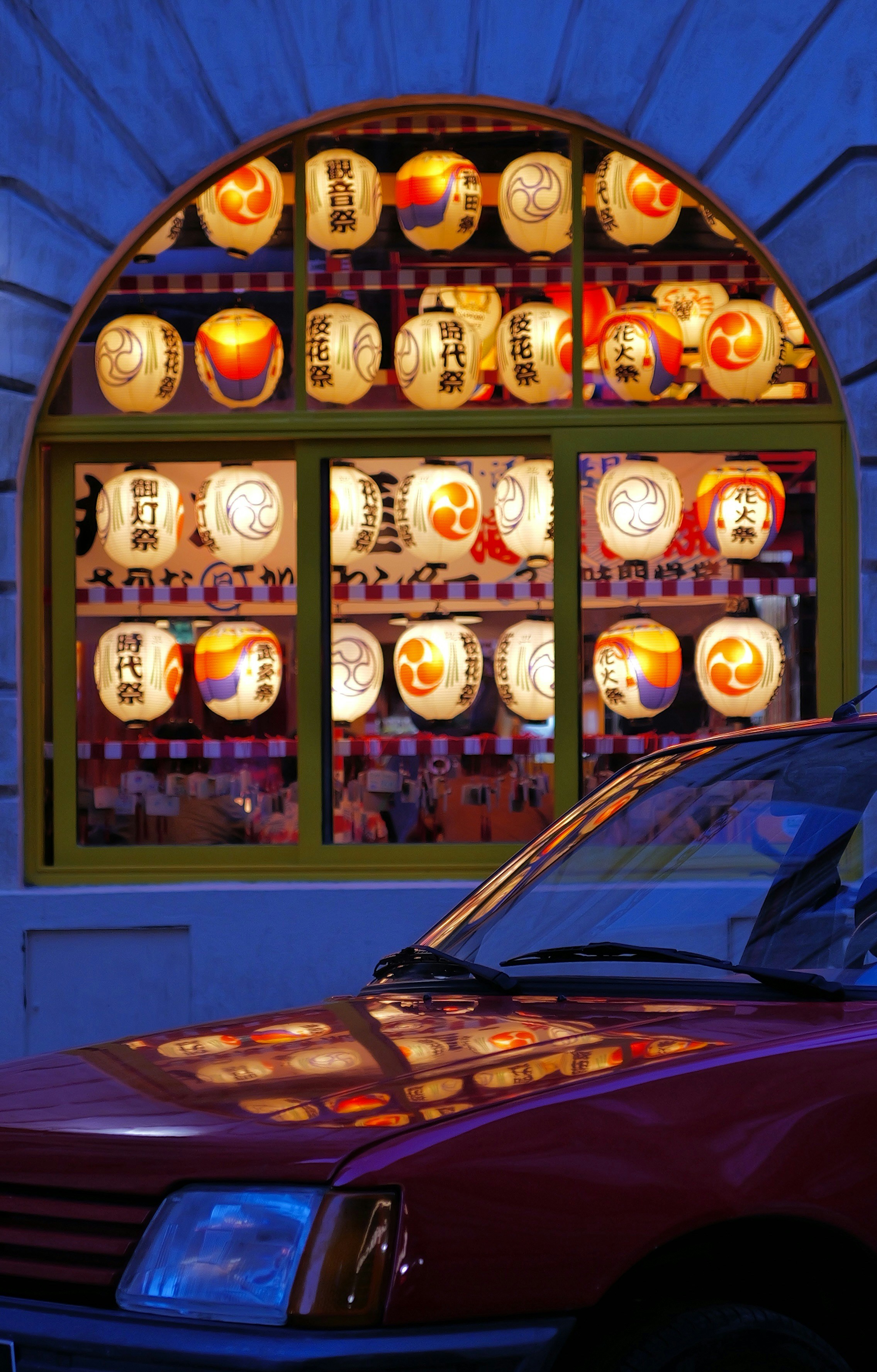 Red car parked in front of illuminated japanese lanterns