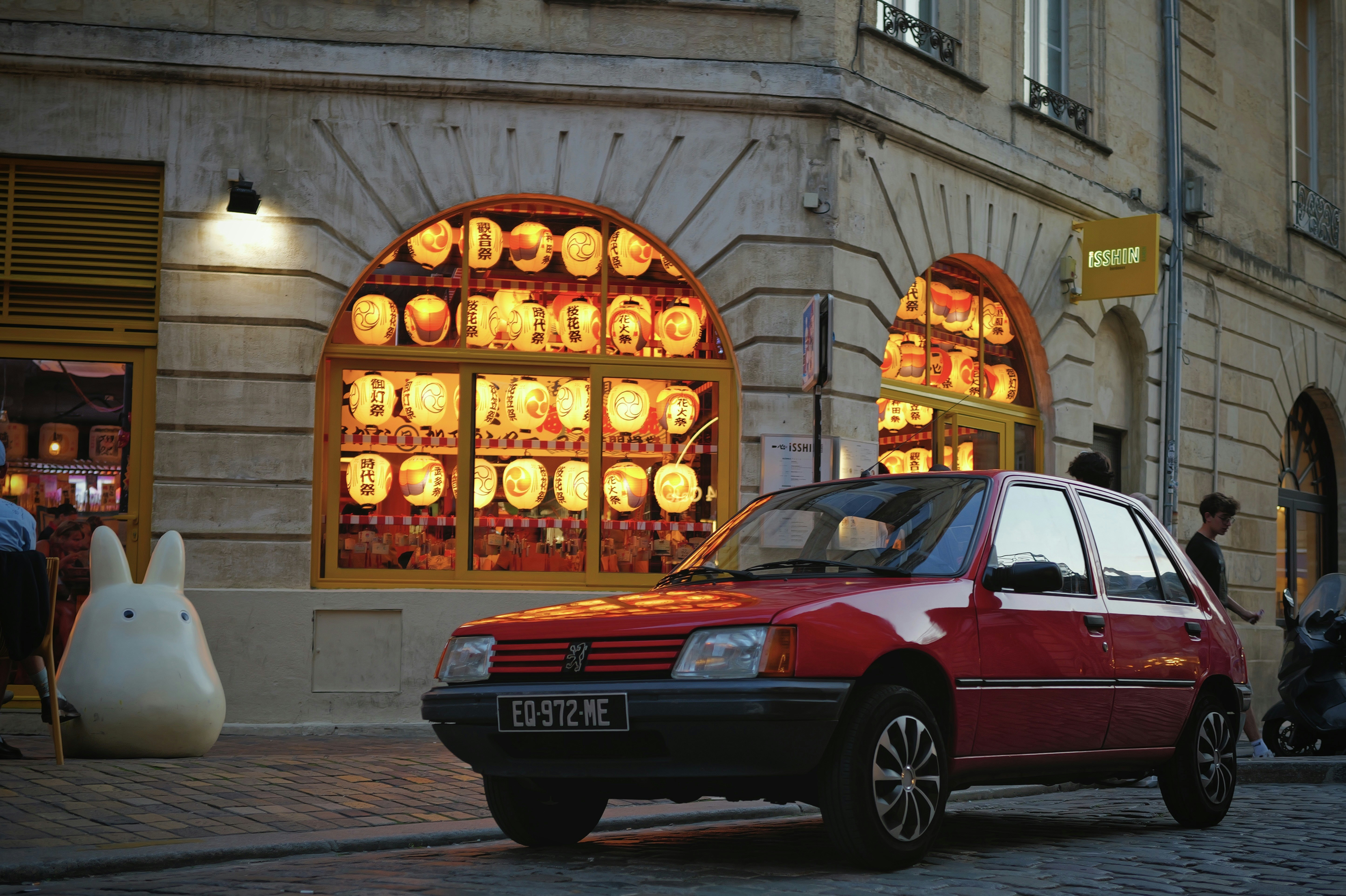 Red car parked outside a building with glowing windows.