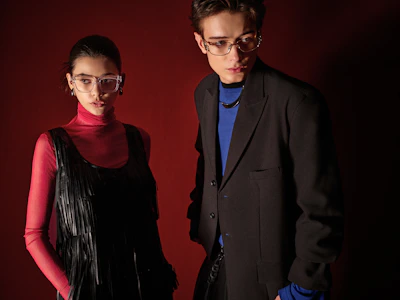 Two models posing in stylish eyeglasses against red background