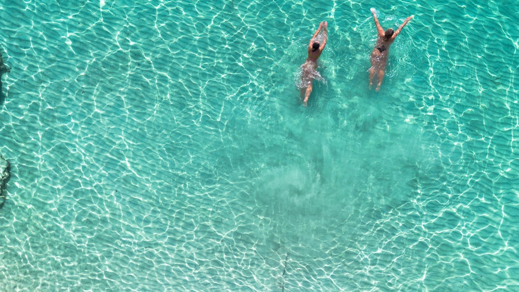 Two women swimming in clear turquoise ocean water.