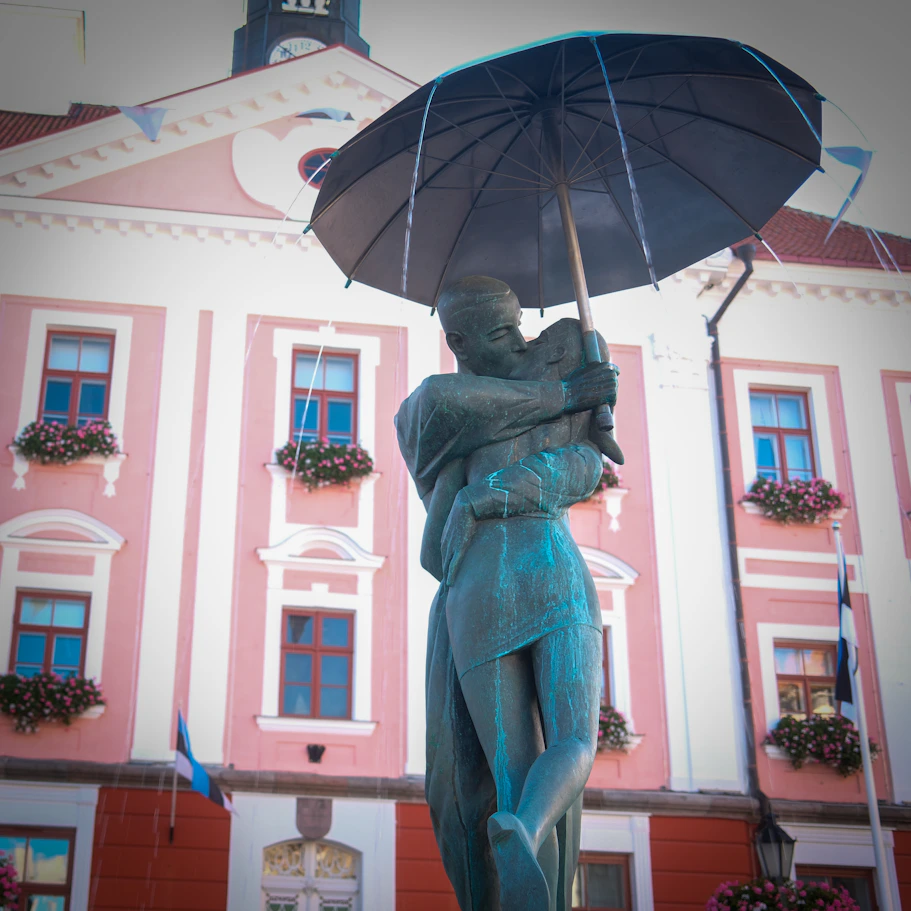 Statue of embracing couple under umbrella with building.