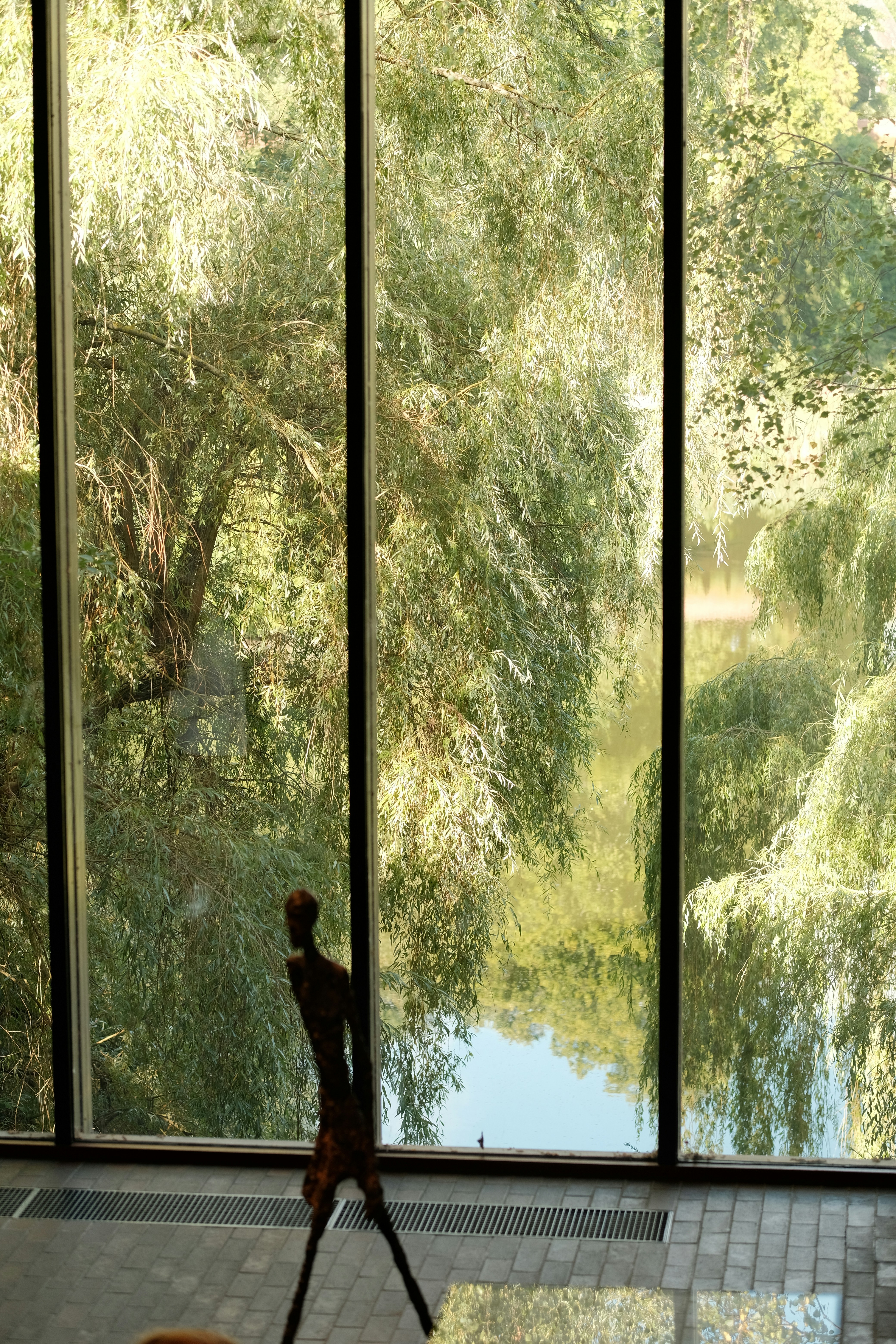 Sculpture in front of large windows overlooking trees.