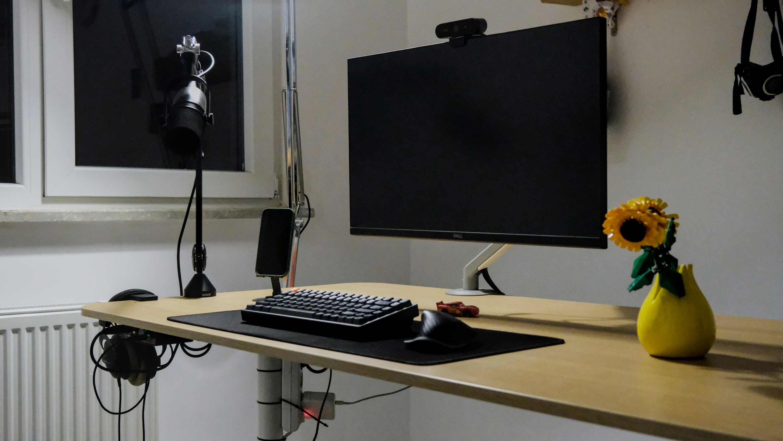 A computer desk with monitor, keyboard, and sunflower