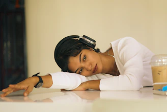 Young woman with headphones rests head on desk.