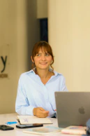 Young woman in light blue shirt at desk with laptop.