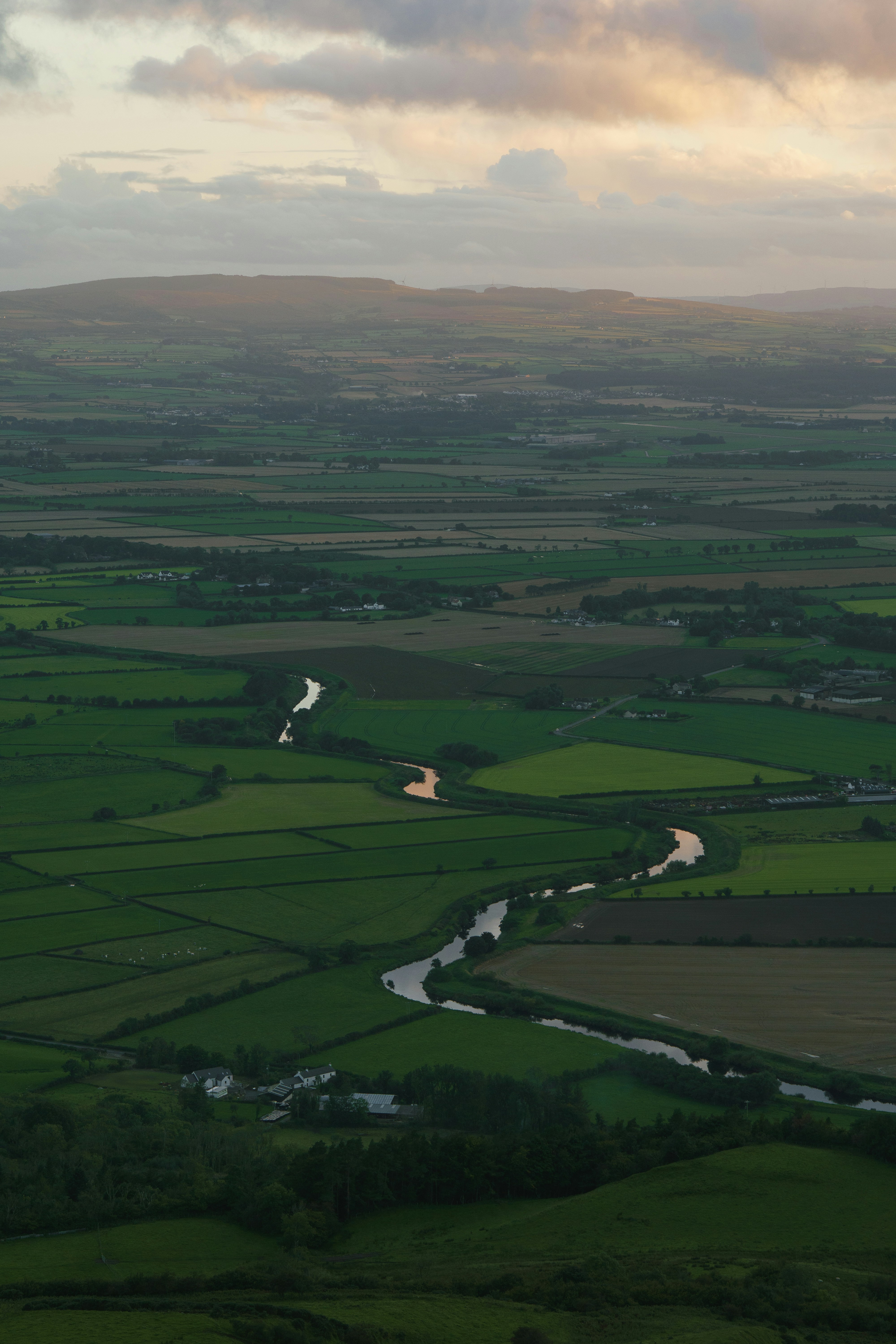 Winding river through green fields under cloudy sky