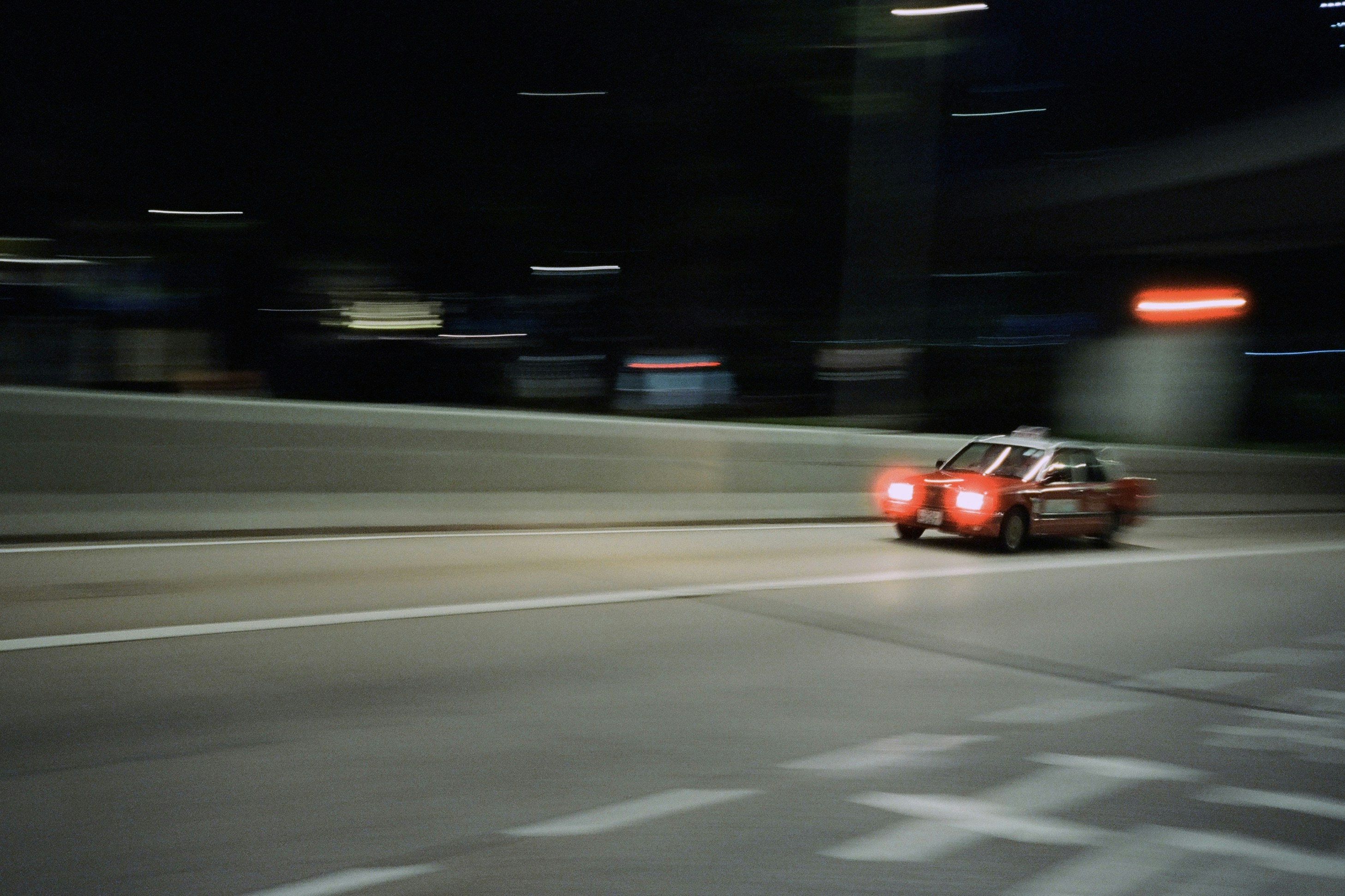 Red car driving on a highway at night.